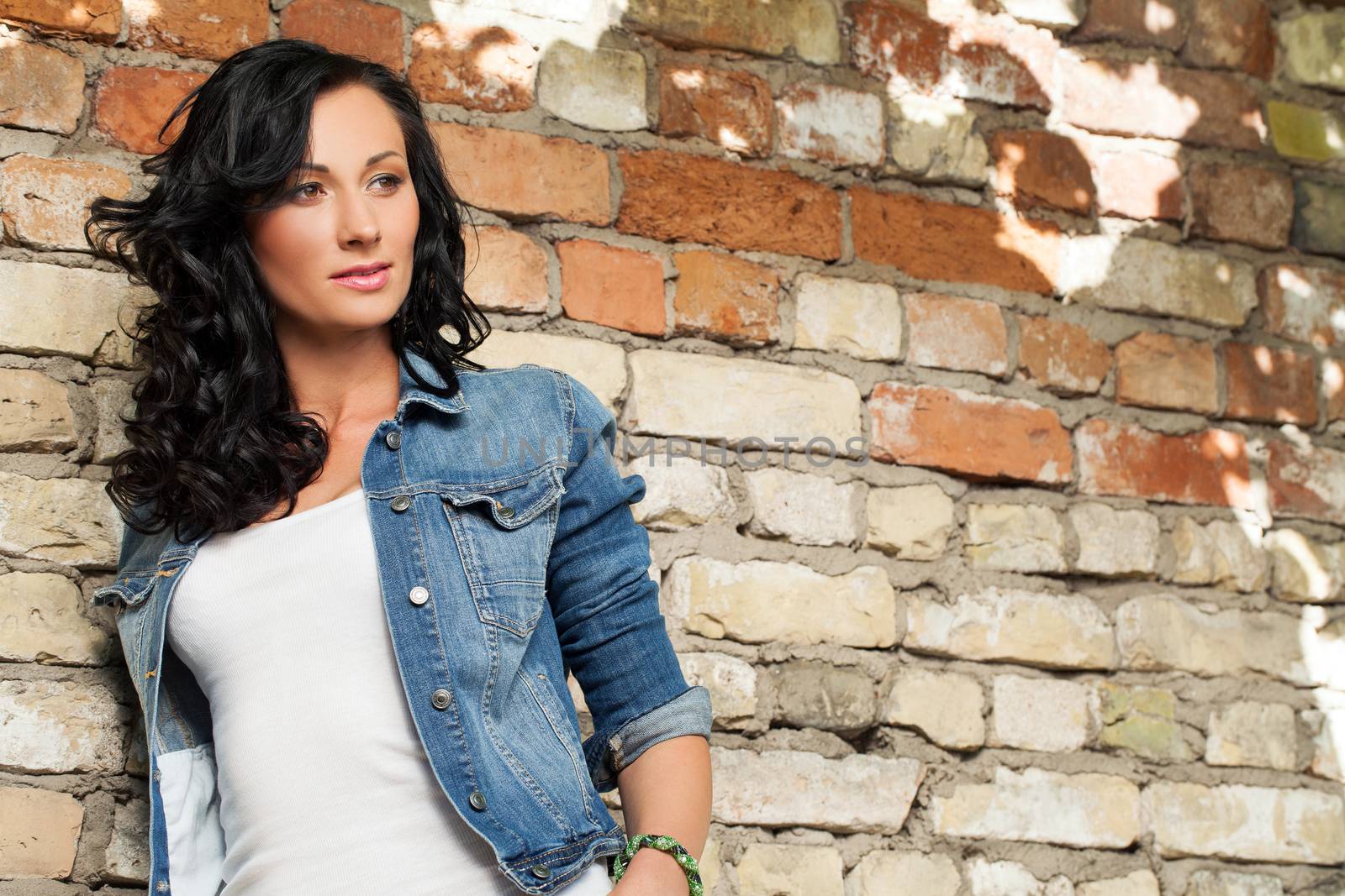 Beautiful young caucasian woman at the brick wall in jeans