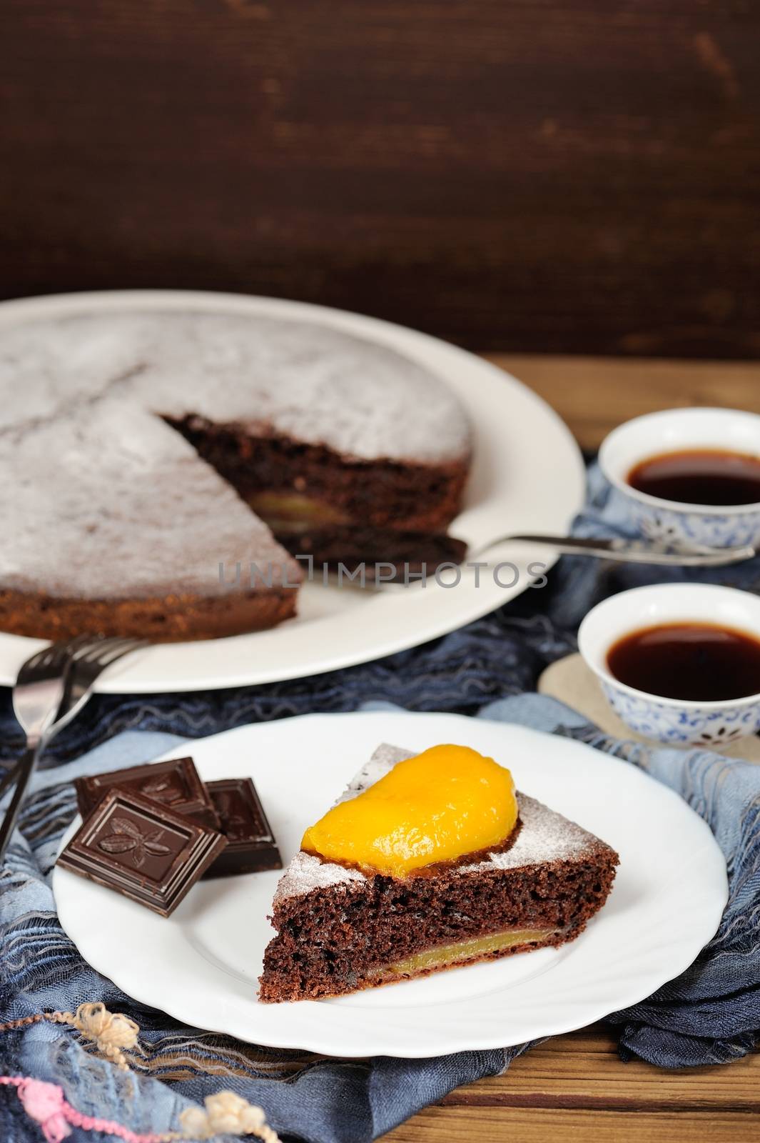 Chocolate cake with mango and black tea on blue cloth with space background vertical