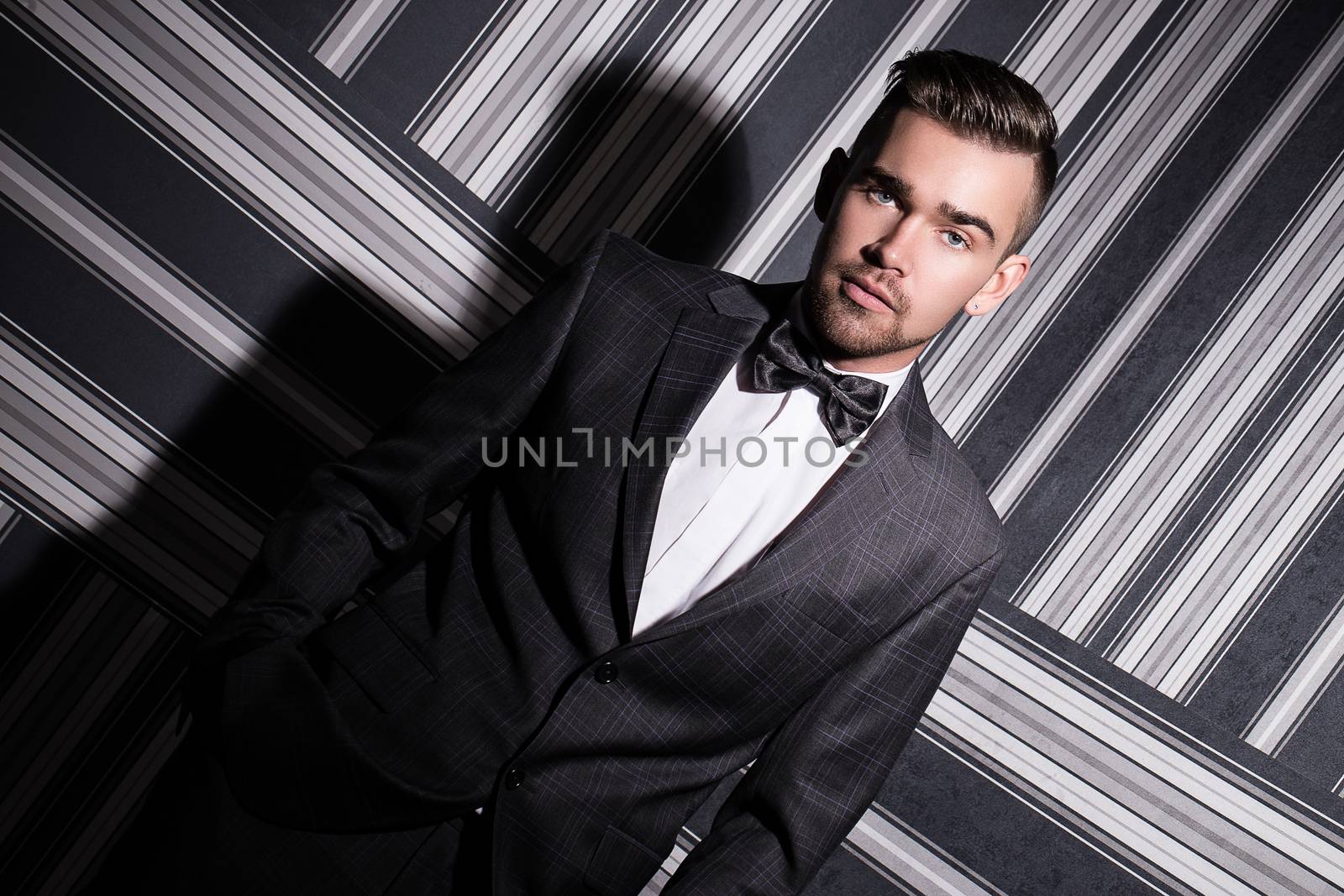 Portrait of a handsome man in a suit and a tie who is posing over a striped background