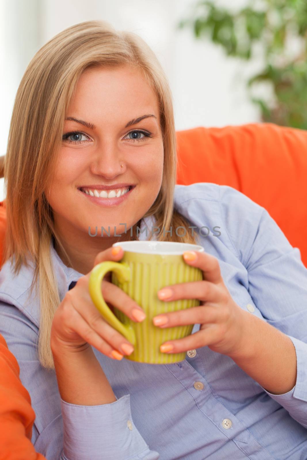 Young blond caucasian woman smiling with mug in orange sofa