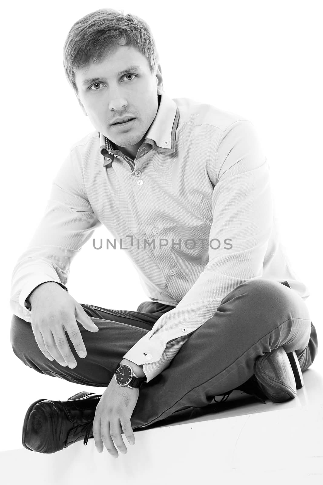 Handsome man in a shirt and trousers is sitting on a cube