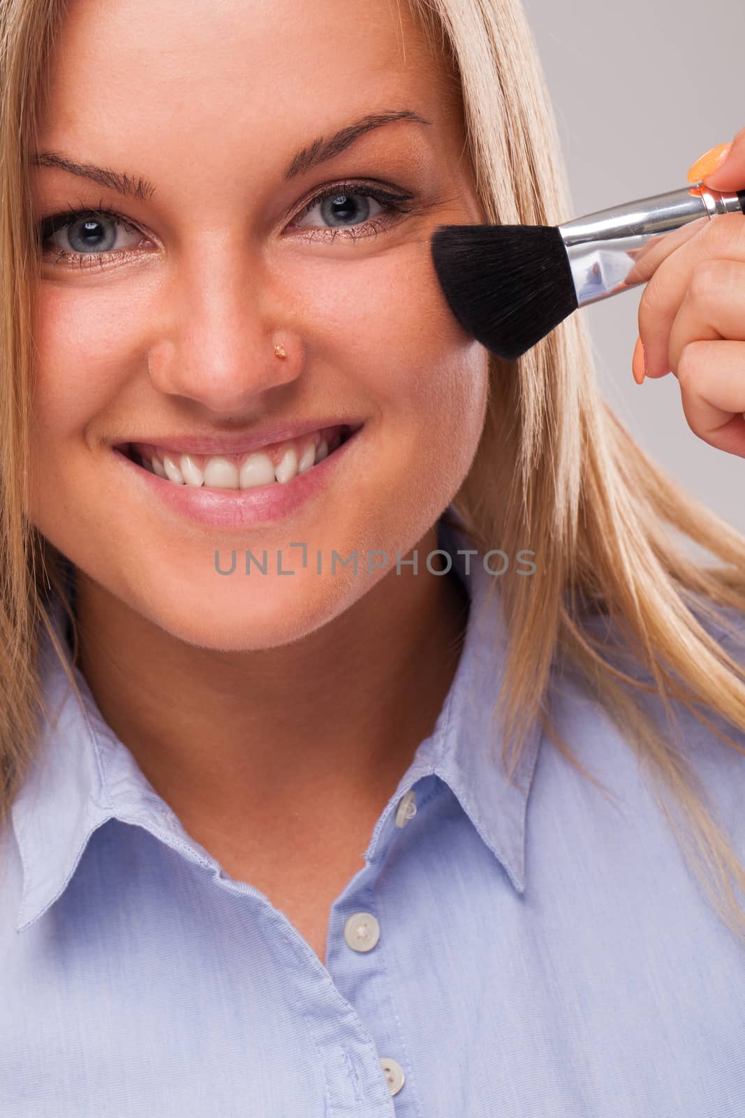 Closeup portrait of young blond caucasian woman smiling with cosmetic brush