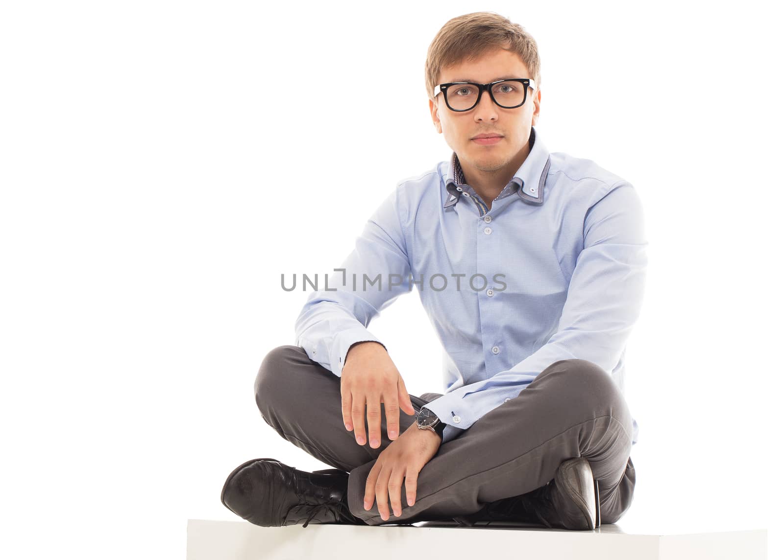 Handsome man in a shirt and trousers is sitting on a cube