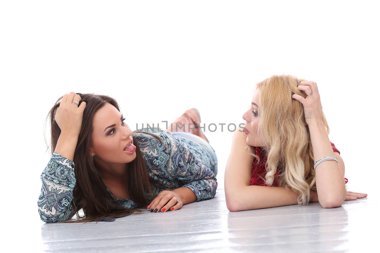A brunette and a blonde girls are lying on the floor and posing over a white background