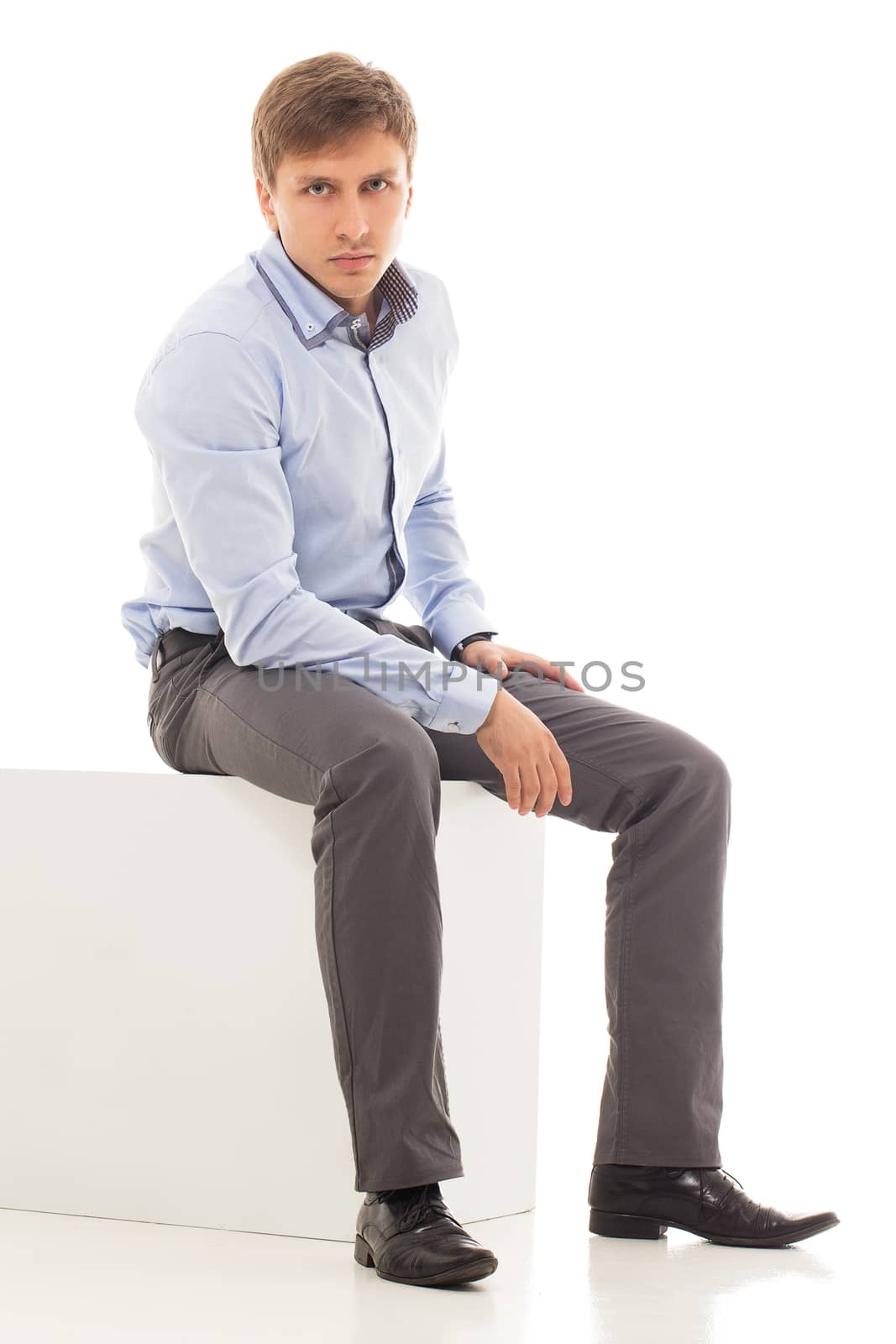Handsome man in a shirt and trousers is sitting on a cube