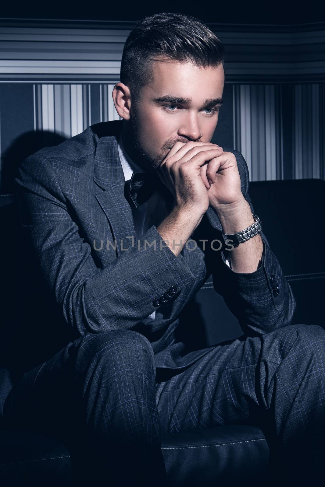 Portrait of a handsome man in a suit who sits in the spotlight over a striped background