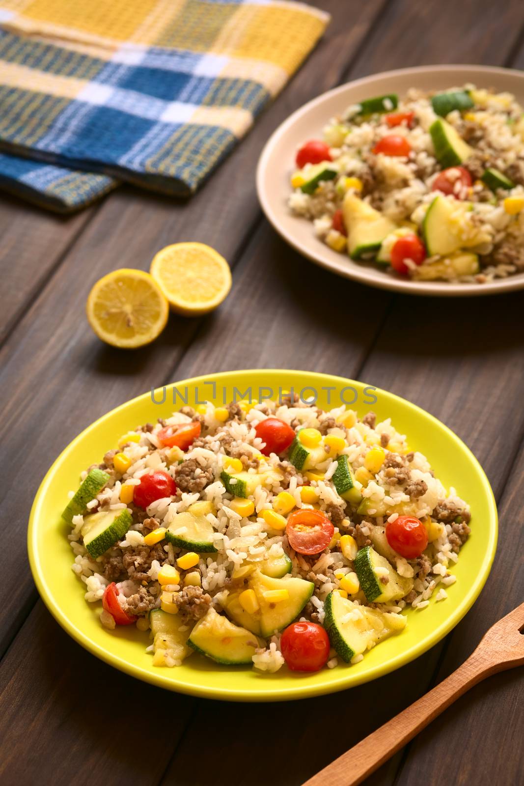 Rice dish with mincemeat and vegetables (sweet corn, cherry tomato, zucchini, onion) served on plate, photographed on dark wood with natural light (Selective Focus, Focus one third into the dish)