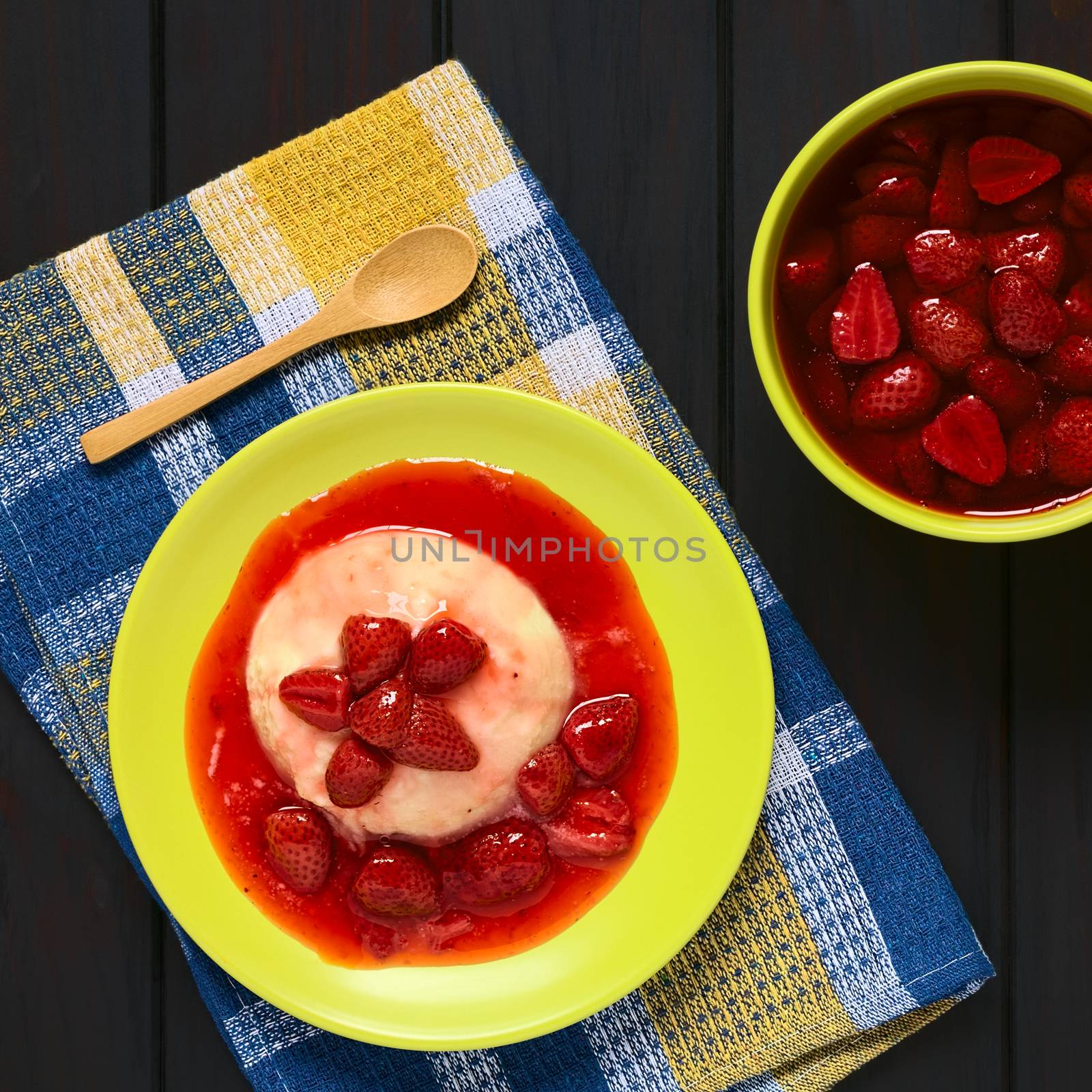 Overhead shot of semolina pudding with strawberry compote served on plate, photographed on kitchen towel on dark wood with natural light