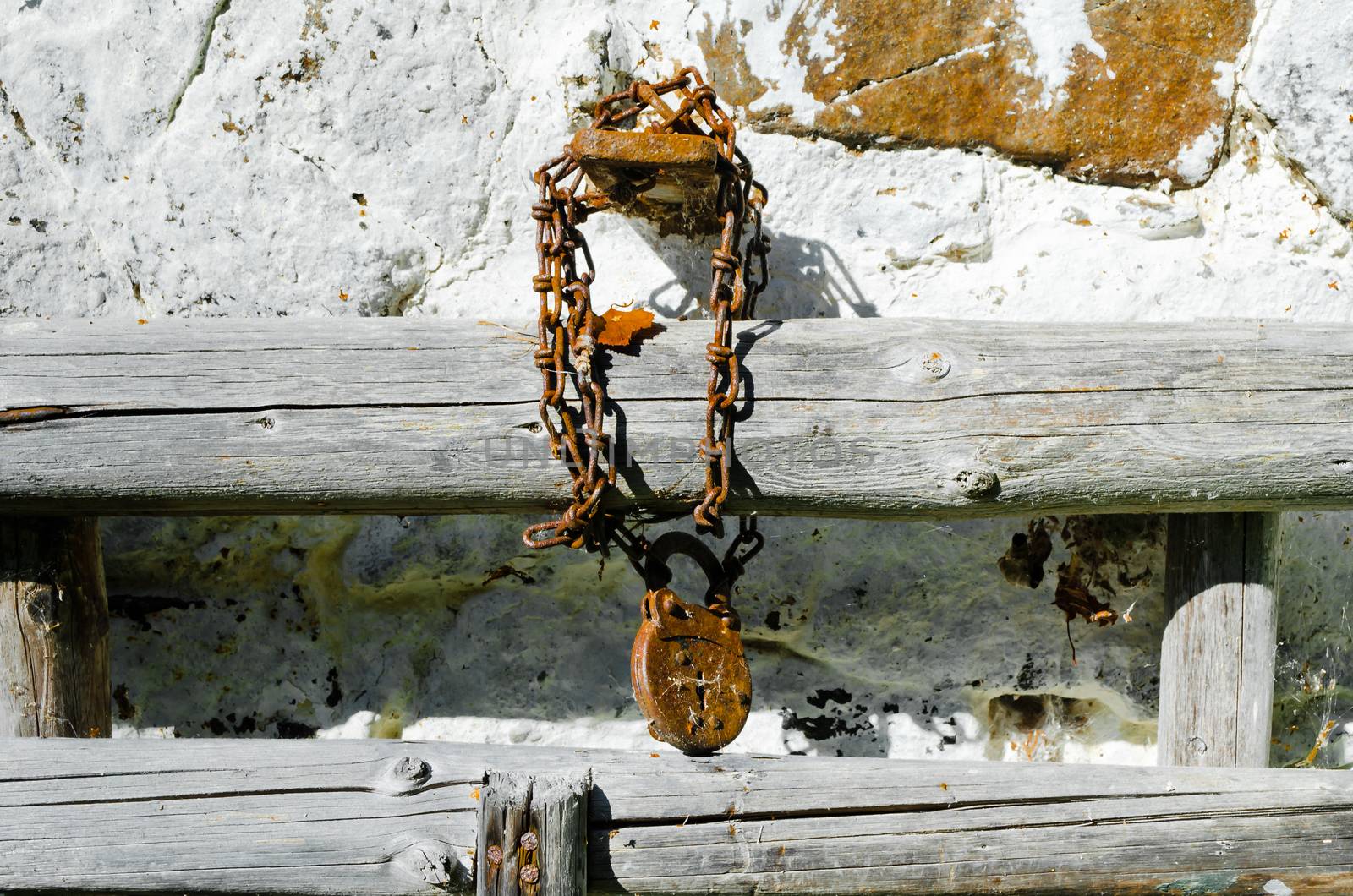 Rusty padlock and chain on the wall of old village house