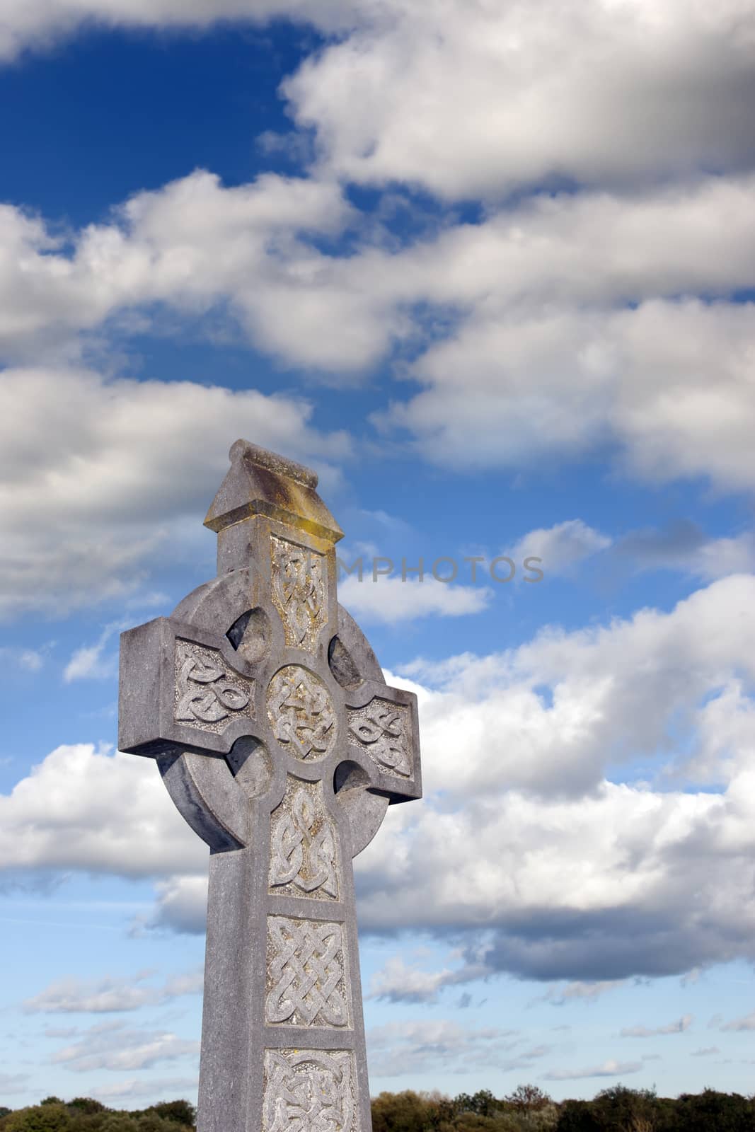 an old celtic cross in an irish graveyard with blue cloudy sky