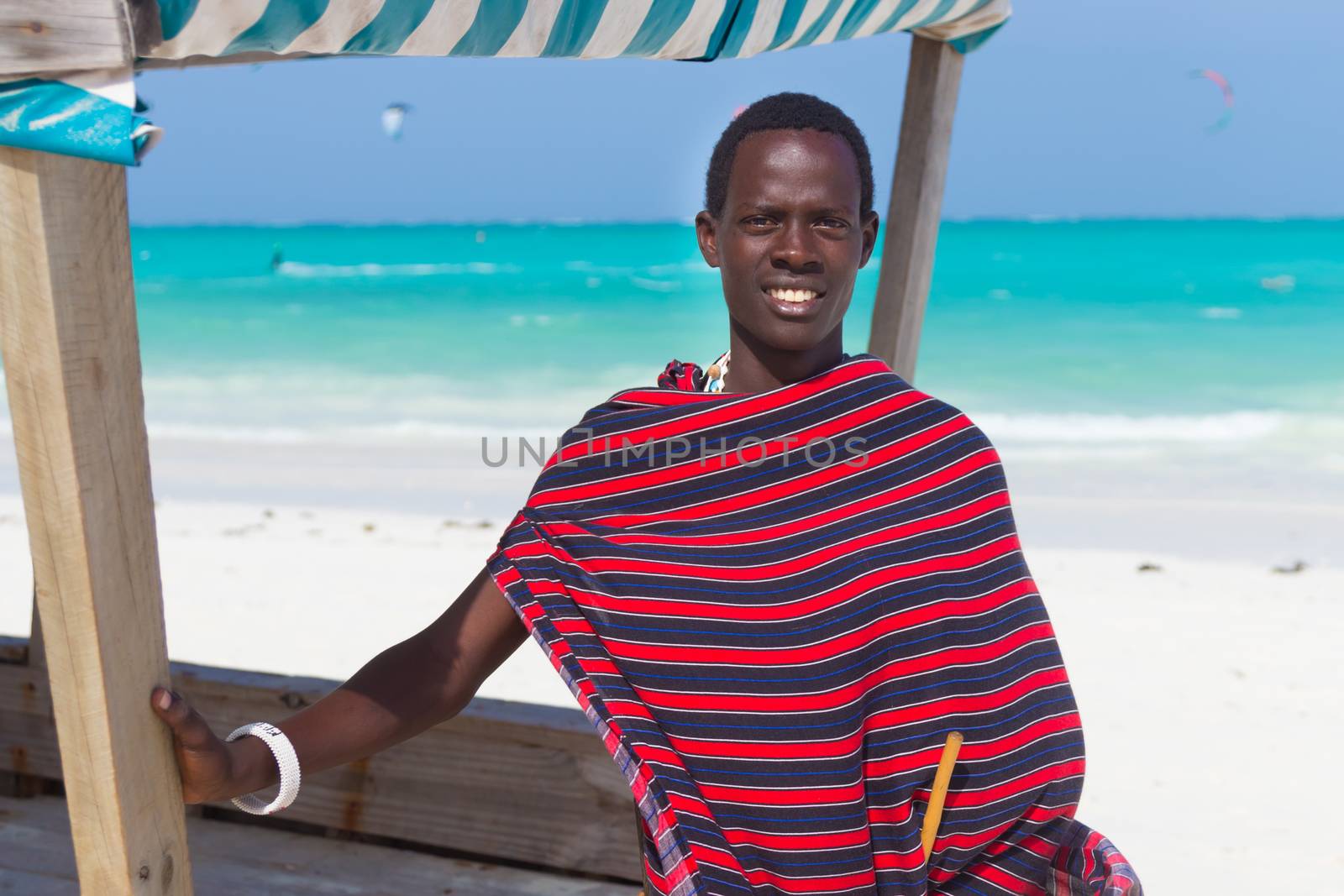 Traditonaly dressed black man on the beach. Maasai warrior on picture perfect tropical sandy beach on Zanzibar, Tanzania, East Africa.