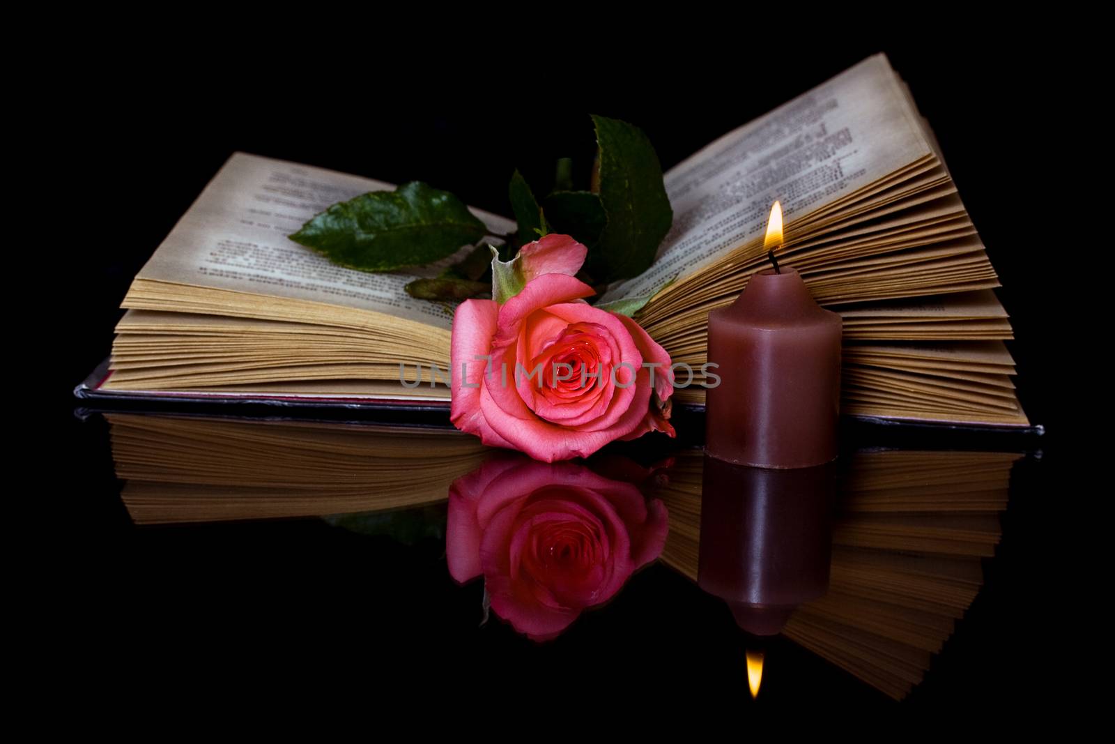 Open book, Rose and a burning candle on a black background