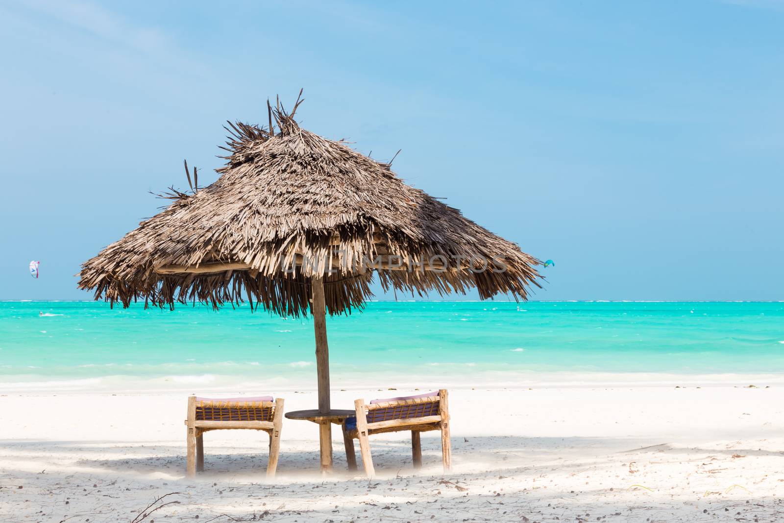 Two wooden dack chairs and umbrella on stunning tropical beach. Turquoise blue lagoon of Paje beach, Zanzibar, Tanzania.