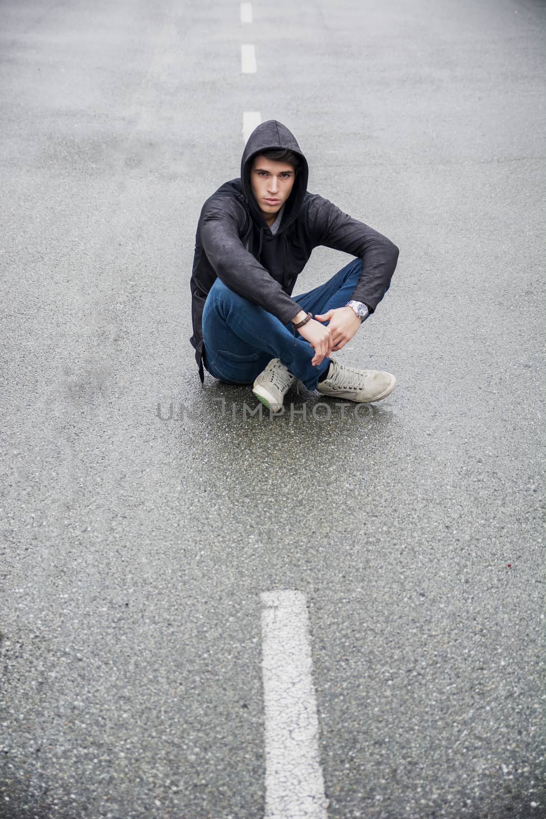 Young man in black hoodie sweater sitting in middle of road by artofphoto
