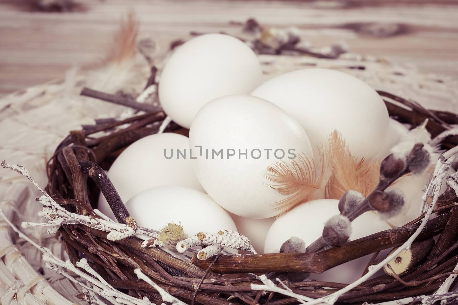 White eggs in nest on a brown wooden table. Done with vintage retro filter. Macro, selective focus