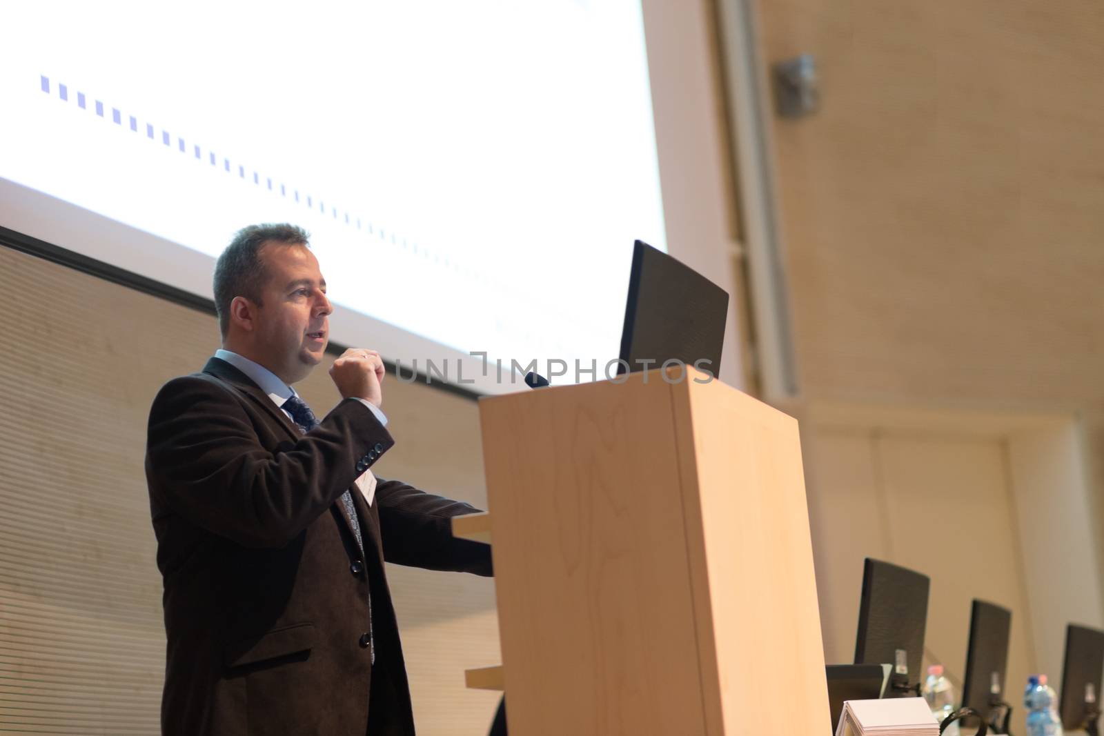 Speaker giving talk on podium at Business Conference. Business and Entrepreneurship. Expert presenting his work in lectures hall.