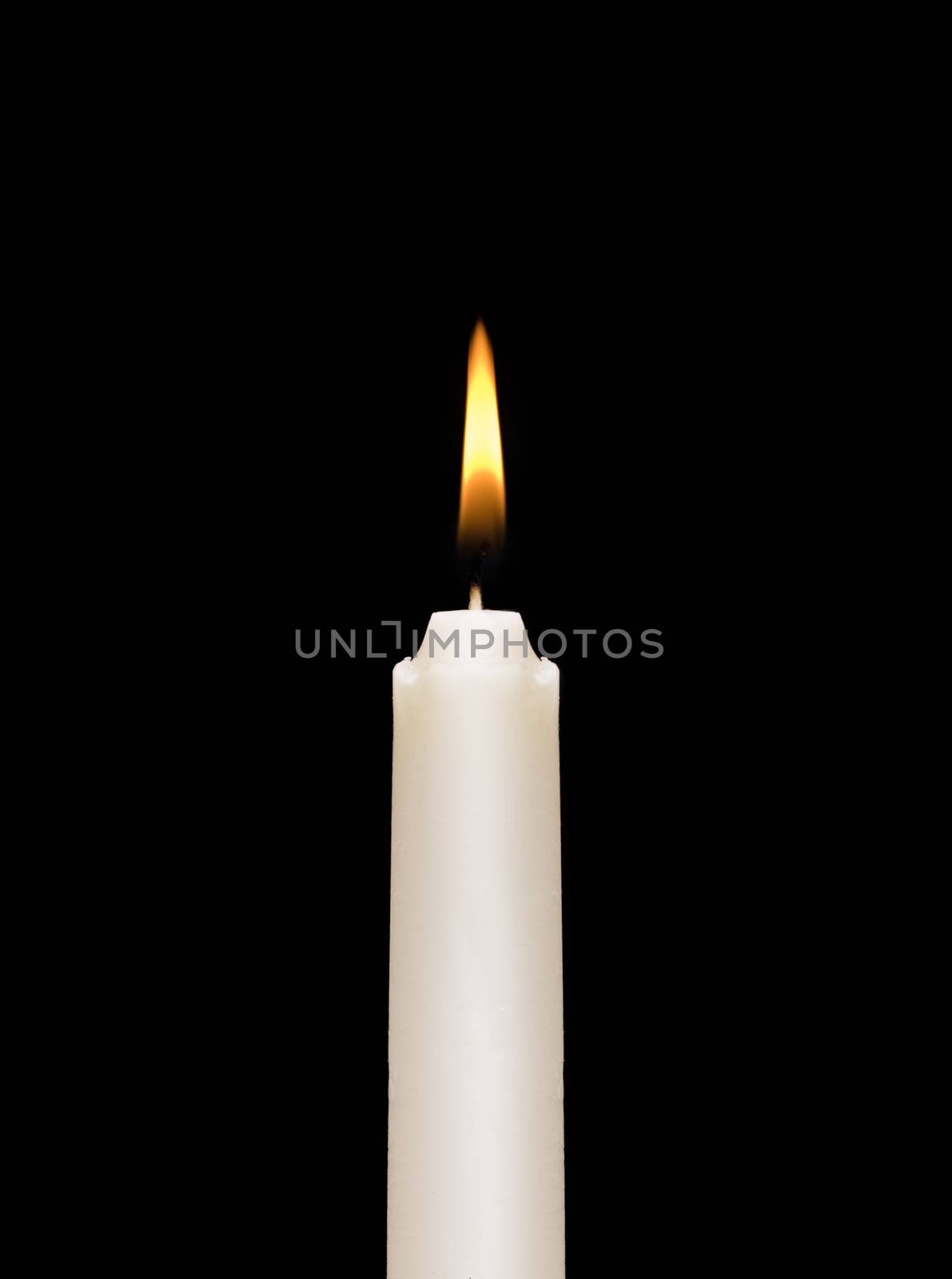 A burning white candle on a black background.