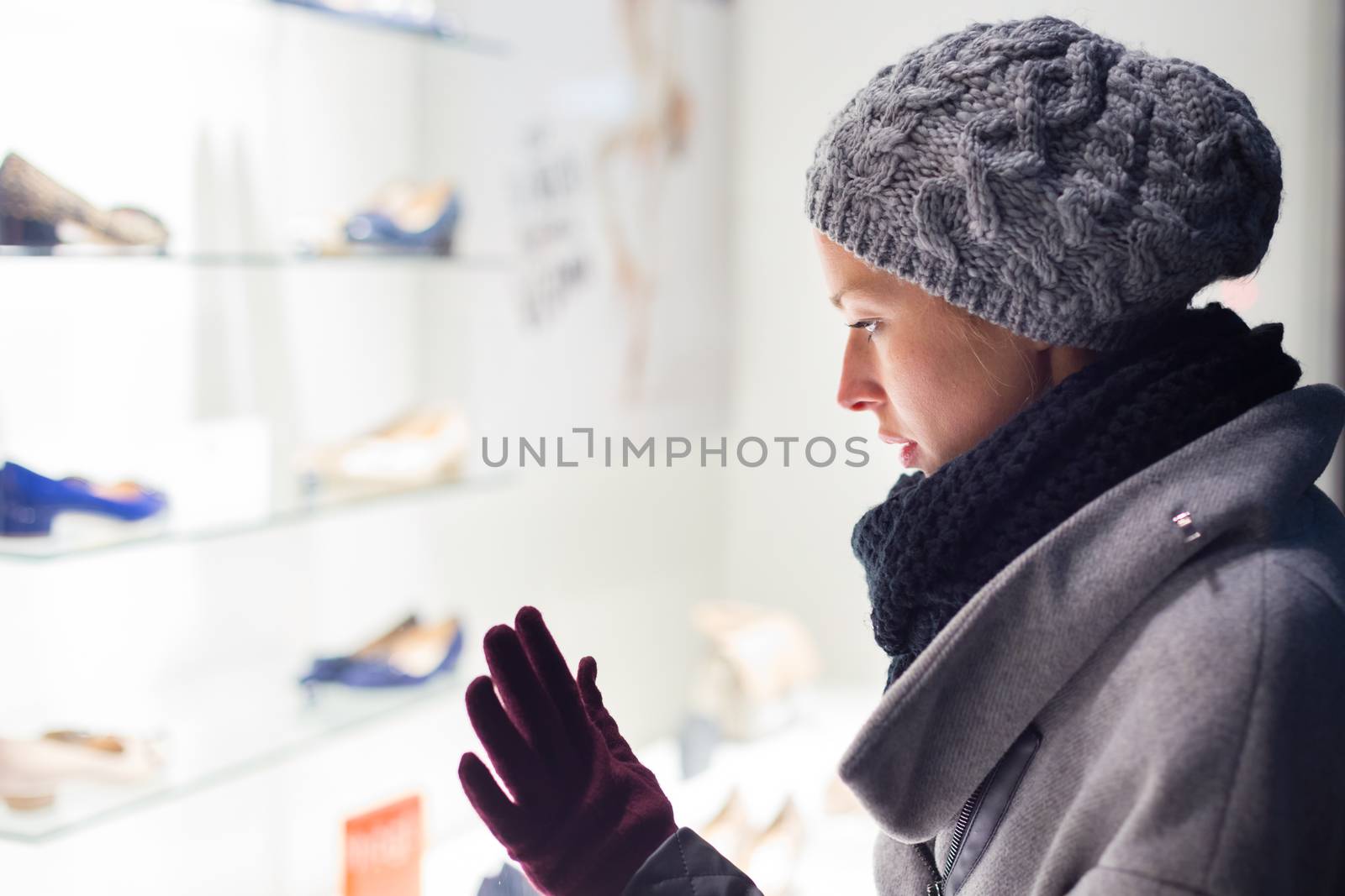 Casualy winter dressed lady window shopping in front of sinfully expensive boutique store dispaly window. Customer woman in shopping street, looking at window, outdoor.