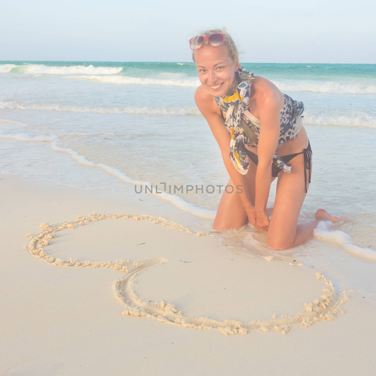 Woman drawing heart on the sand. by kasto