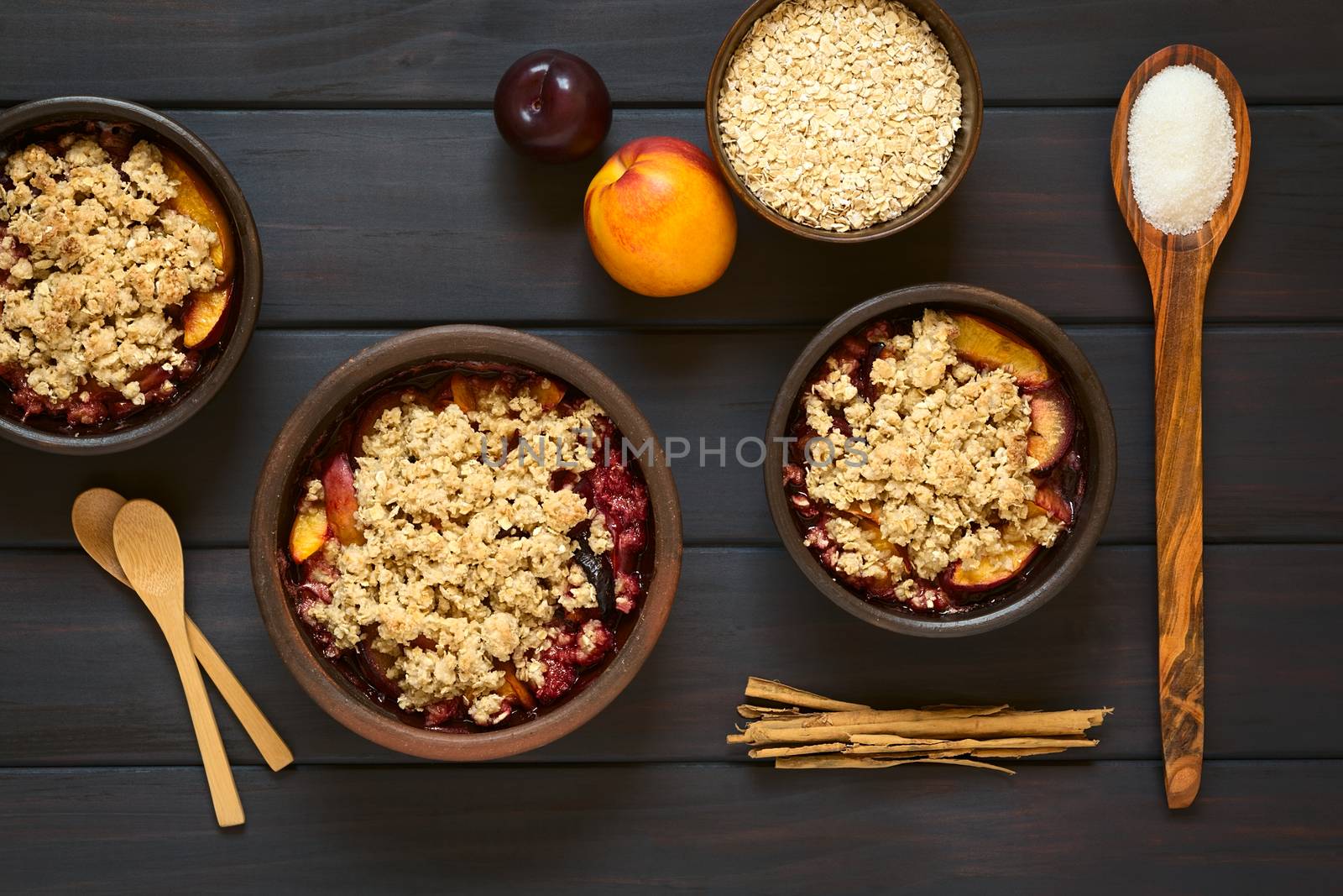 Overhead shot of rustic bowls filled with baked plum and nectarine crumble or crisp, photographed on dark wood with natural light