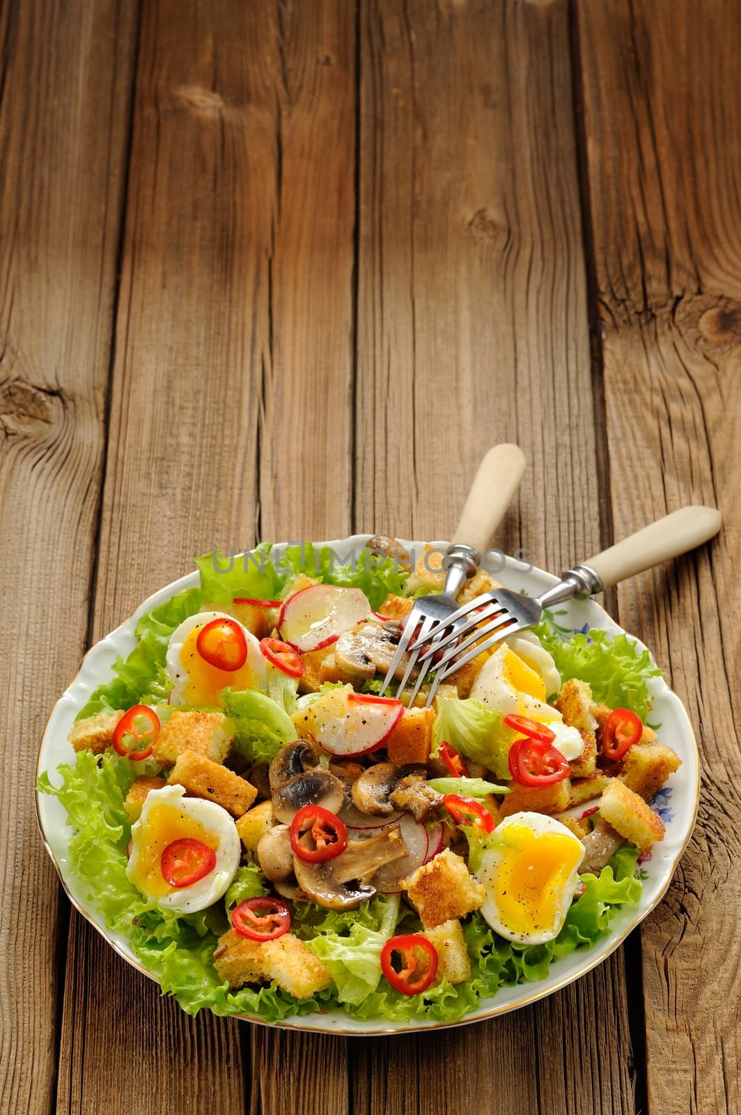Salad Caesar with mushrooms, eggs, chili and radish with two forks on wooden background with space vertical