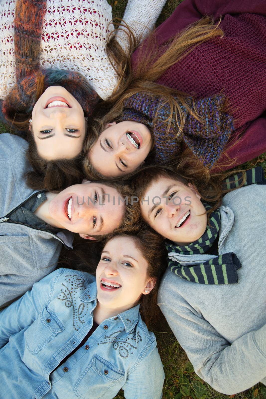 Group of five Caucasian teenagers laying down on grass together
