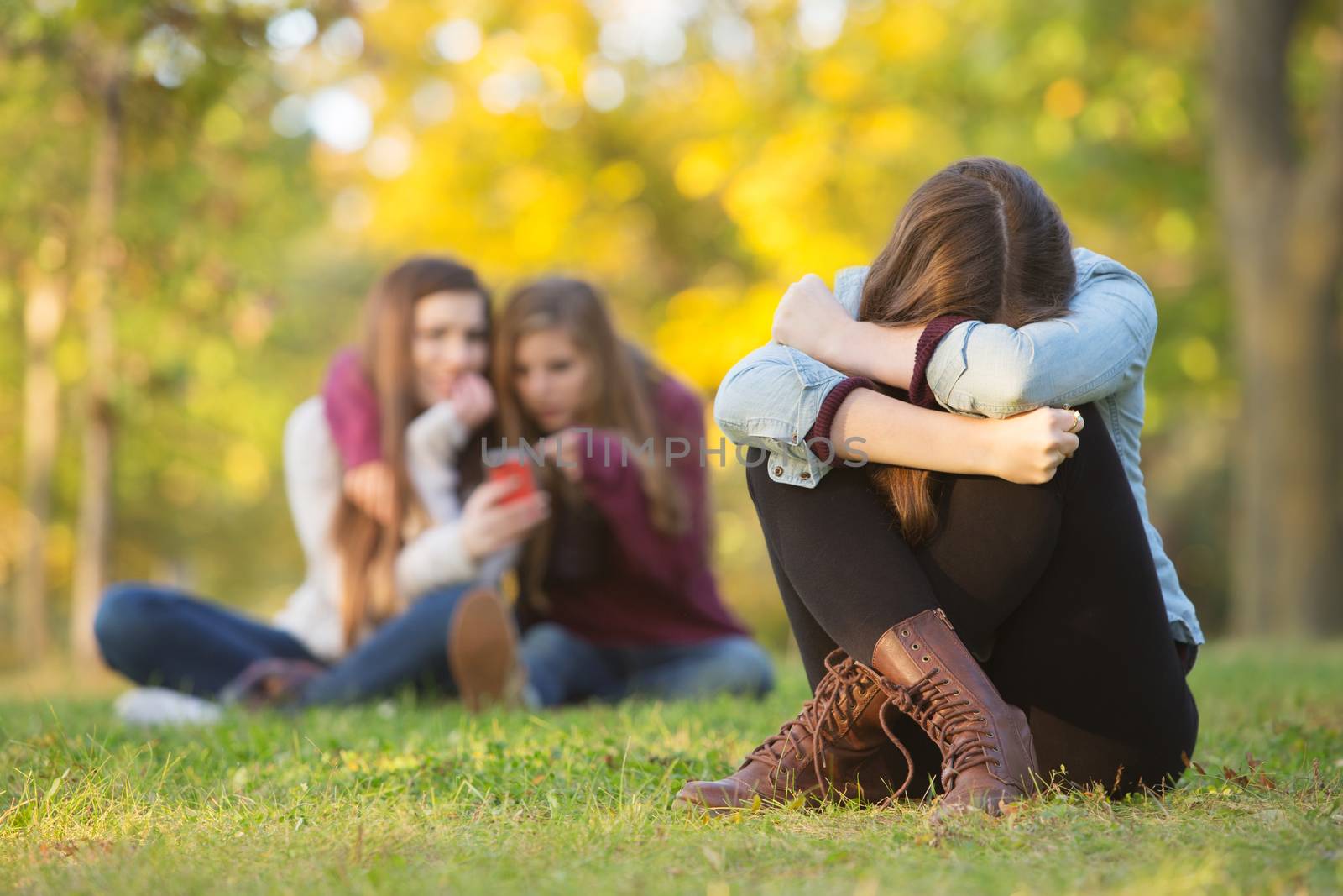 Sad teenage woman sitting with head down near laughing group