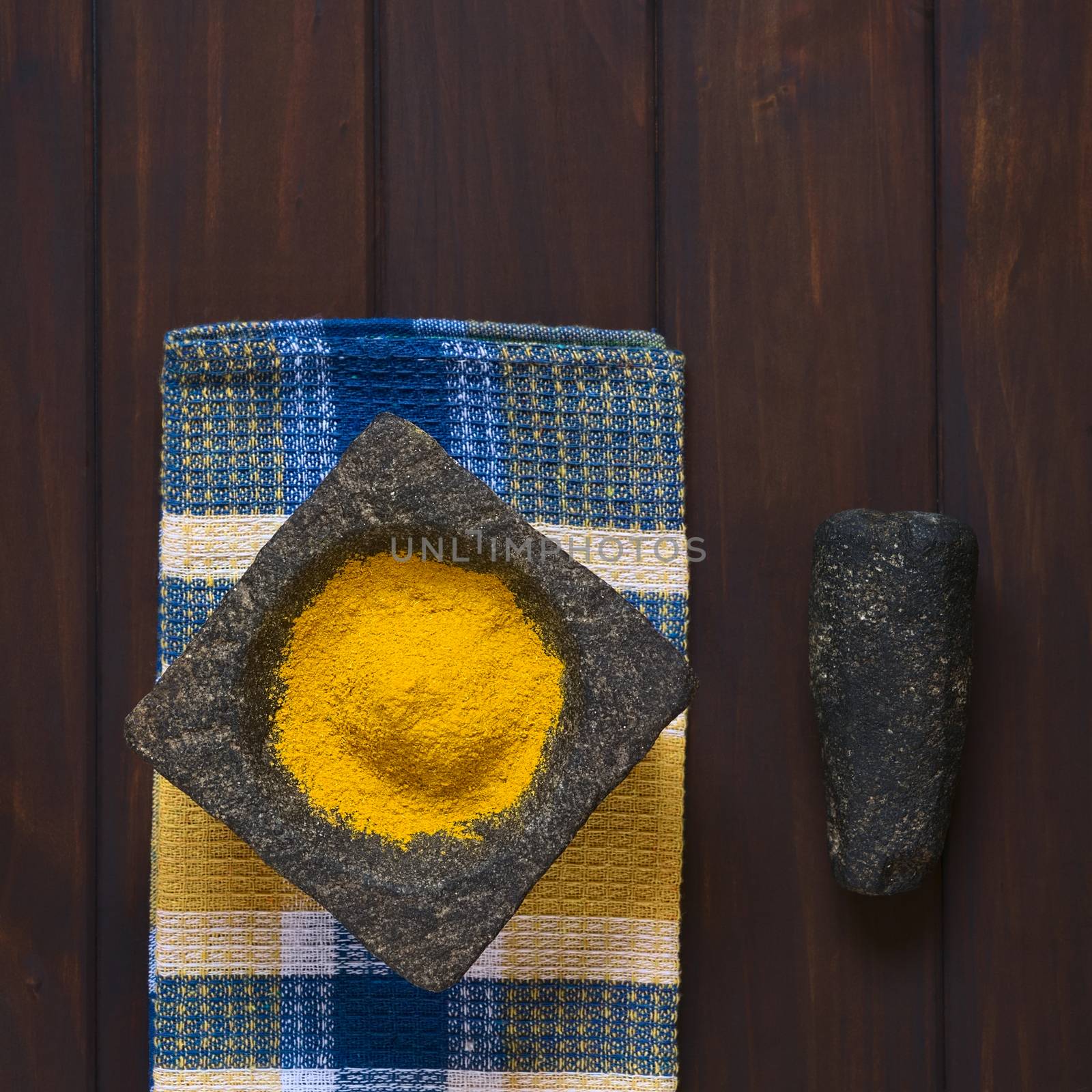 Overhead shot of curry powder spice in mortar with pestle on the side, photographed on dark wood with natural light 