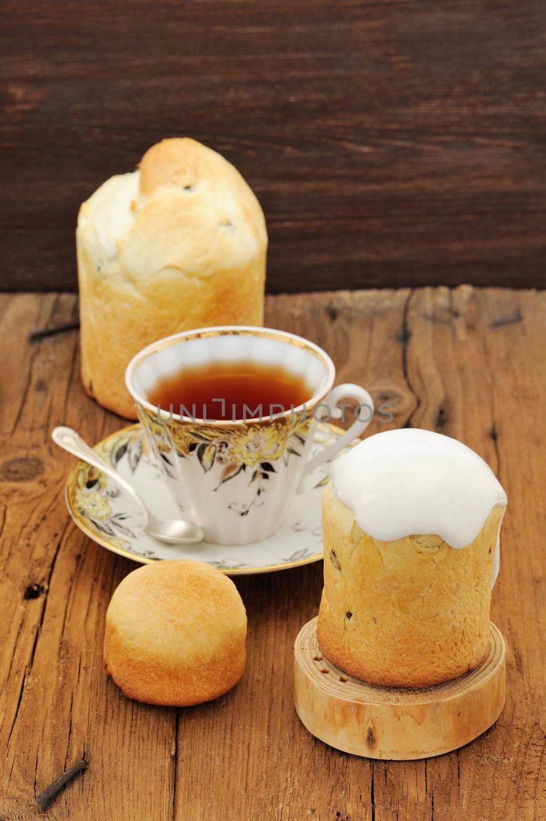 Kulichi, traditional Russian Easter cake with icing, cup of black tea on wooden background vertical