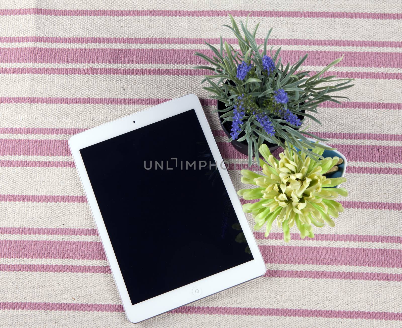 The composition of the tablet on a rustic rug with flowers.