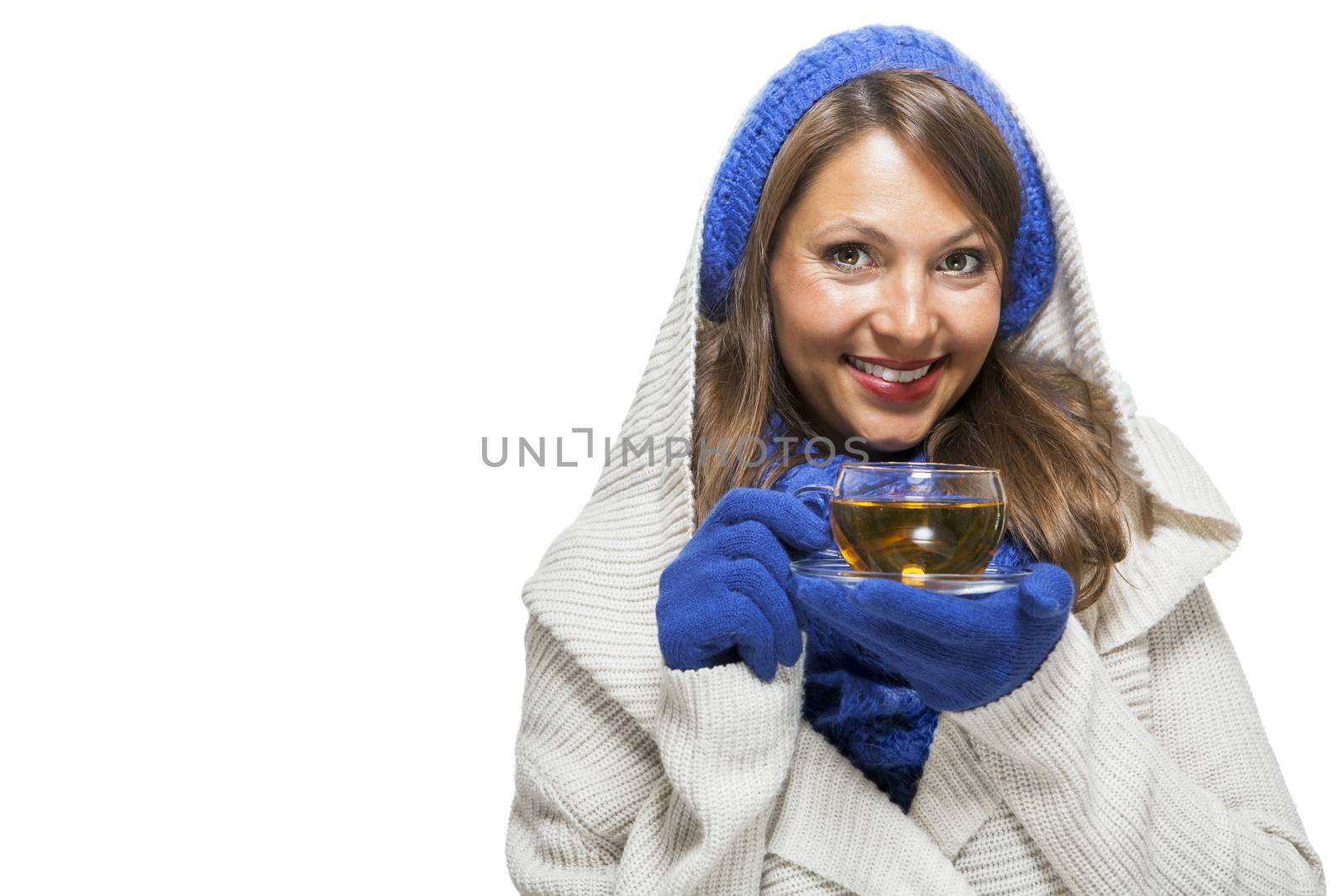 Fashionable young woman in a blue knitted winter ensemble and cowl neck jersey sipping a cup of hot tea with a smile in an effort to keep warm, isolated on white