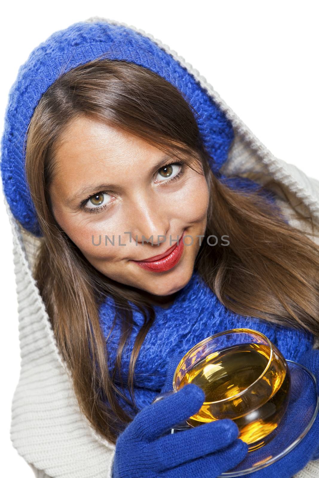 Fashionable young woman in a blue knitted winter ensemble and cowl neck jersey sipping a cup of hot tea with a smile in an effort to keep warm, isolated on white