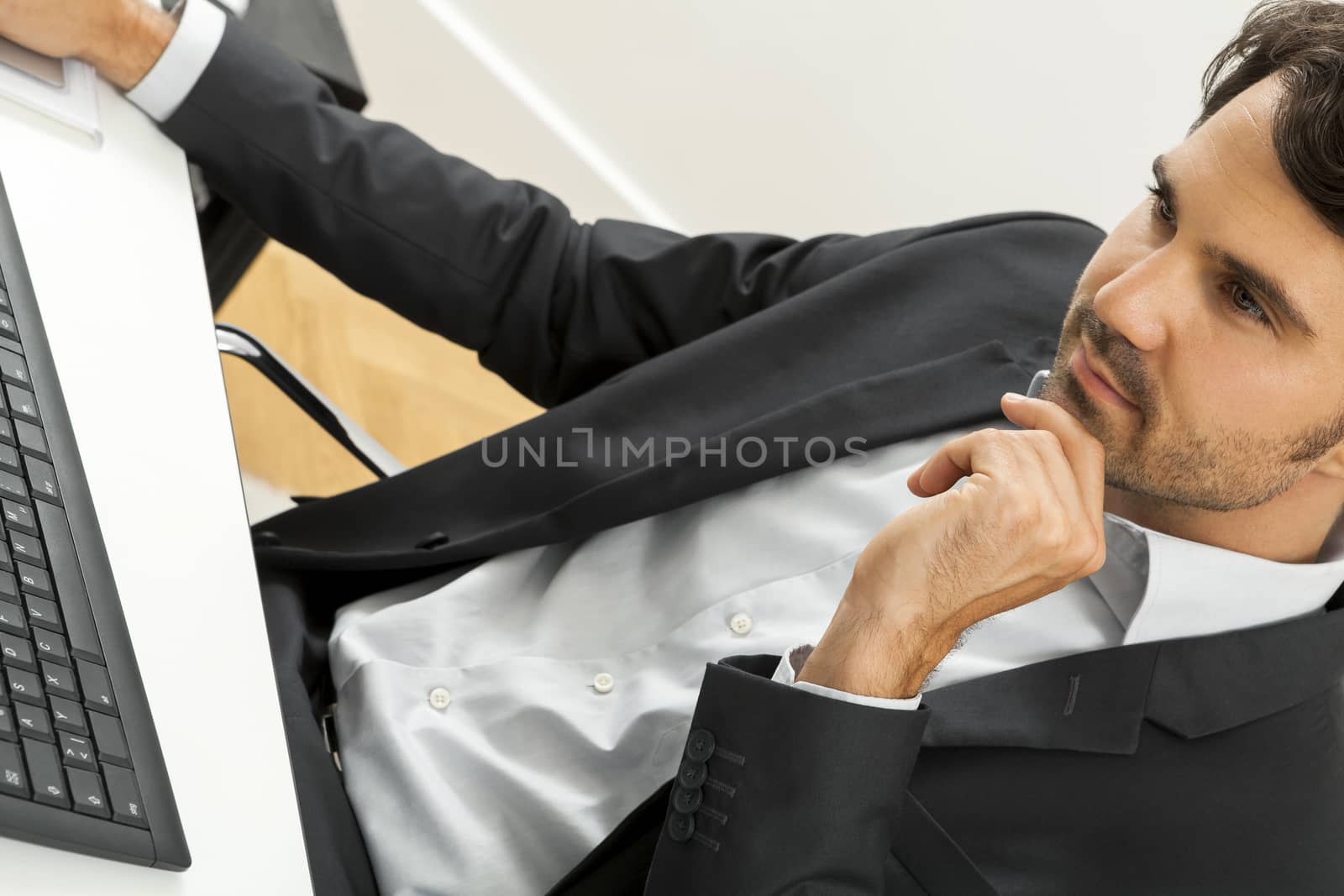 Stylish businessman in a suit sitting at his desk in the office chatting on the phone with a view of his blank computer monitor