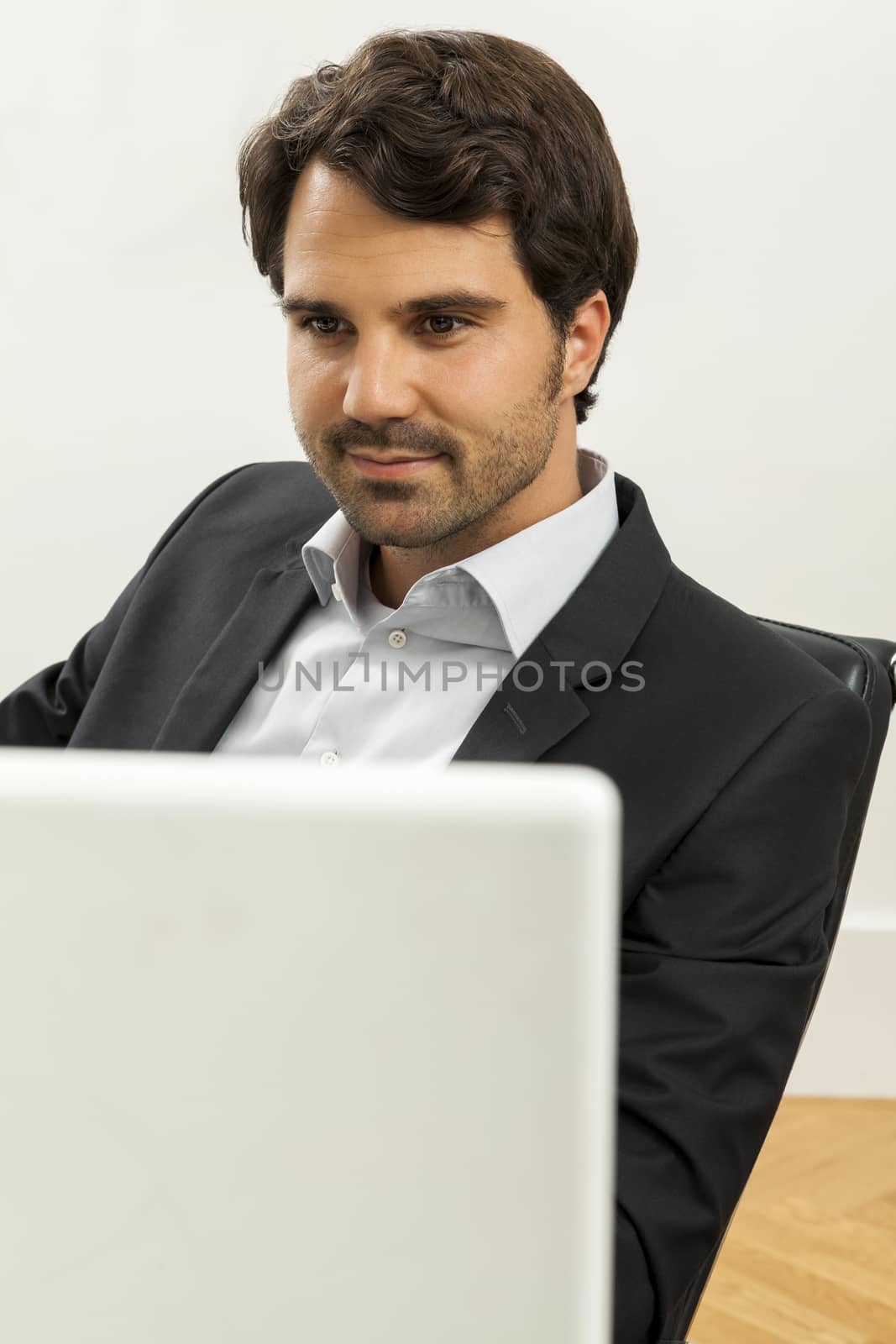 Stylish businessman in a suit sitting at his desk in the office chatting on the phone with a view of his blank computer monitor