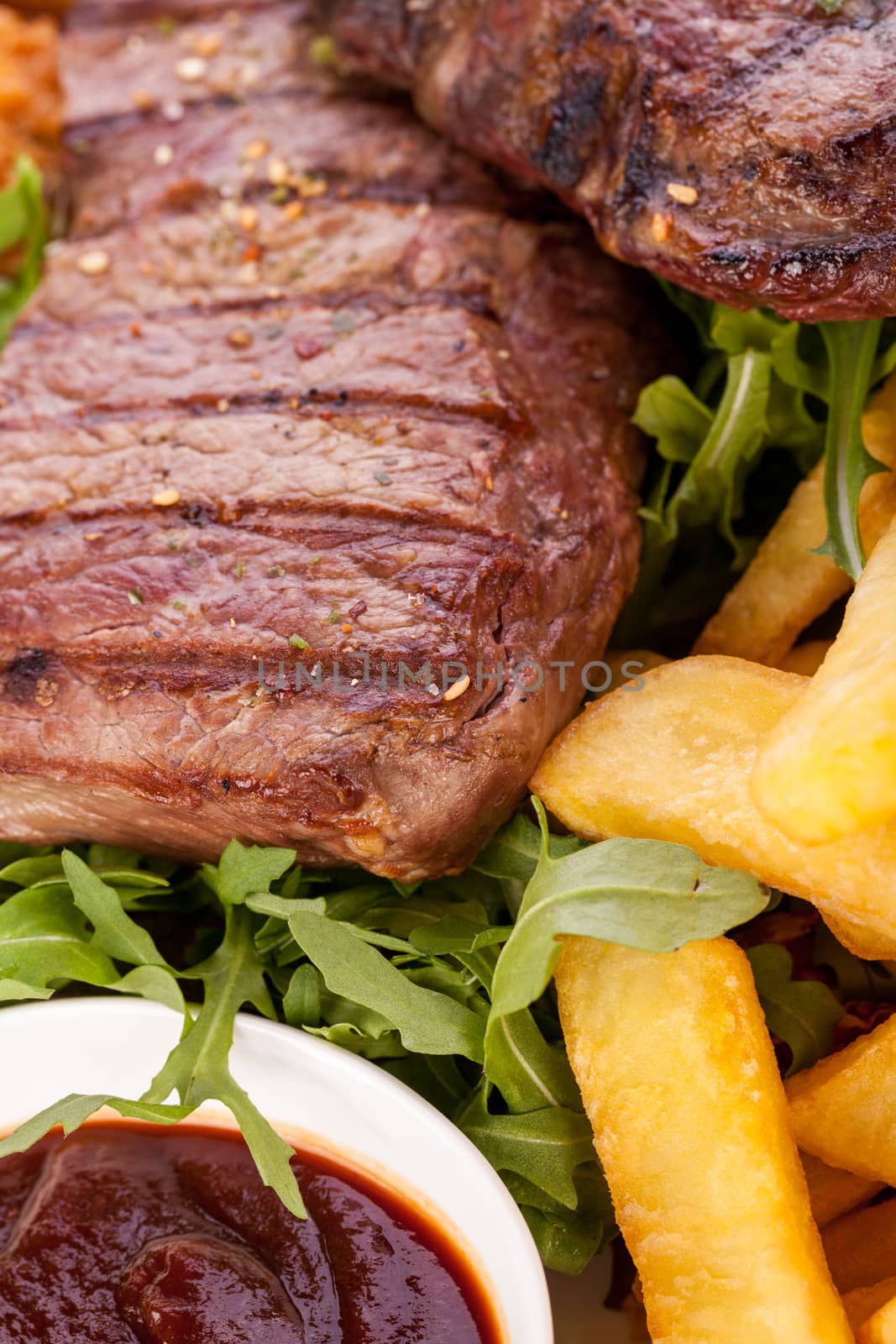 Wholesome platter of mixed meats including grilled steak, crispy crumbed chicken and beef on a bed of fresh leafy green mixed salad served with French fries and chutney or BBQ sauce in a dish