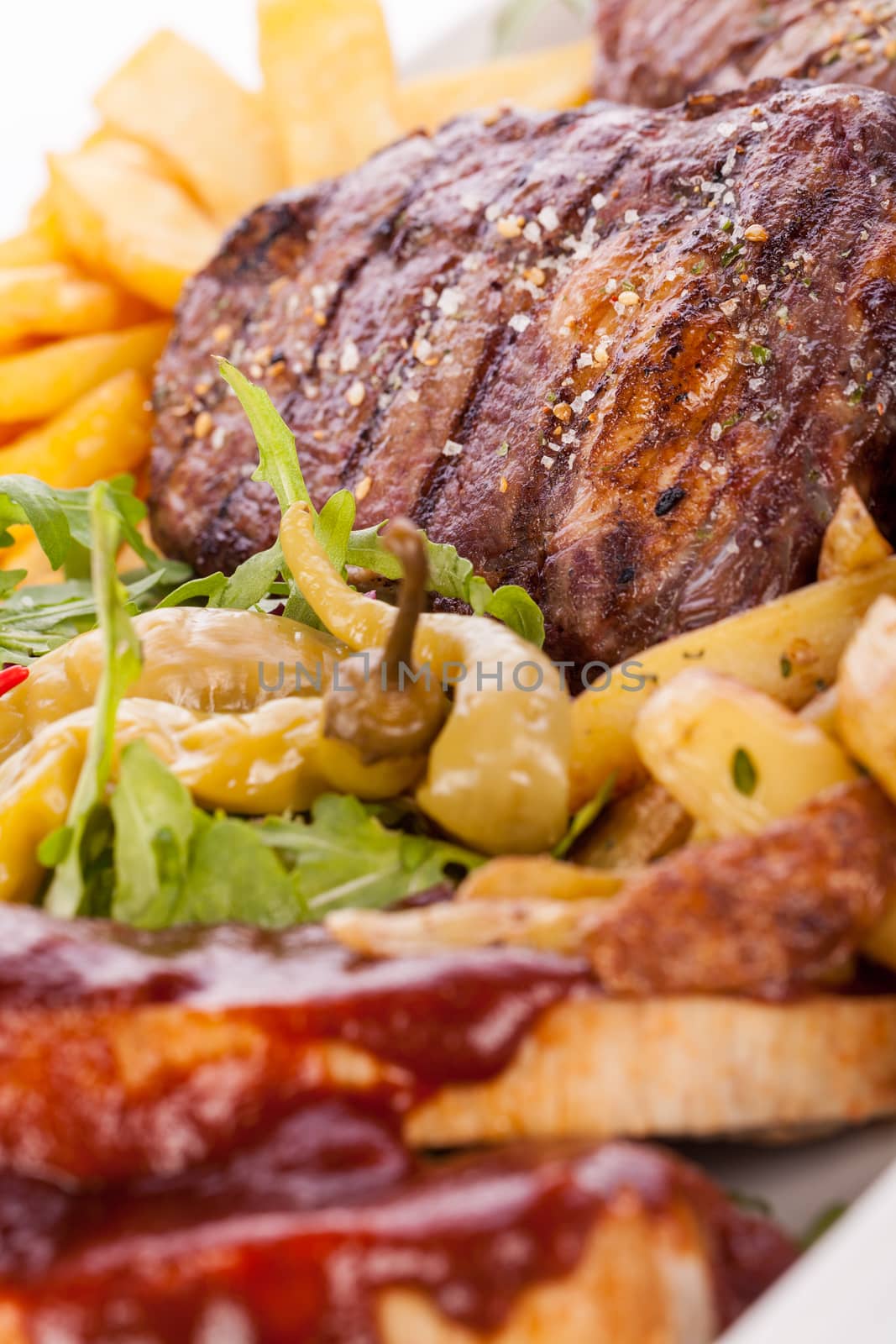 Wholesome platter of mixed meats including grilled steak, crispy crumbed chicken and beef on a bed of fresh leafy green mixed salad served with French fries and chutney or BBQ sauce in a dish