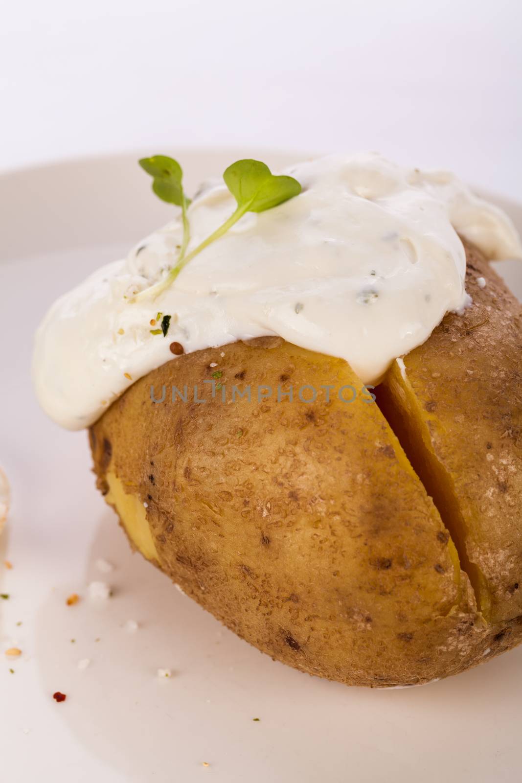 Overhead view of a healthy oven baked jacket potato with sour cream sauce garnished with endive leaves and fresh herbs