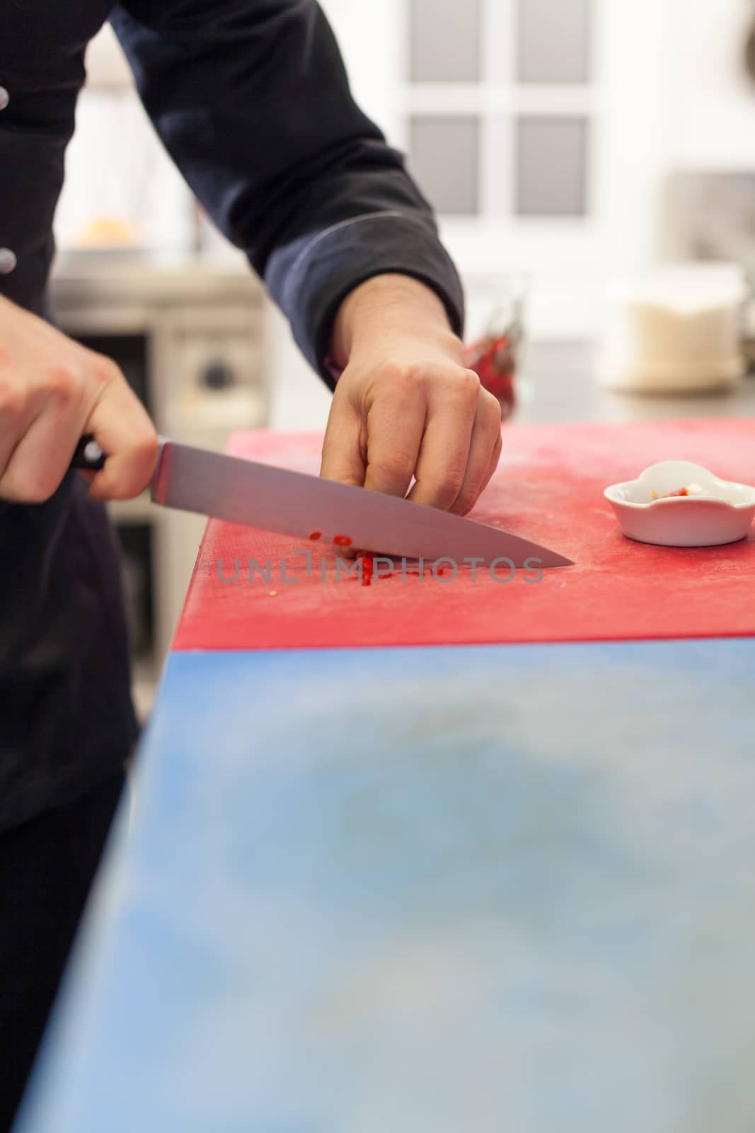 Chef dicing red hot chili peppers on a chopping board in a commercial kitchen for use as a spicy flavouring in his recipes as he cooks the evening meal