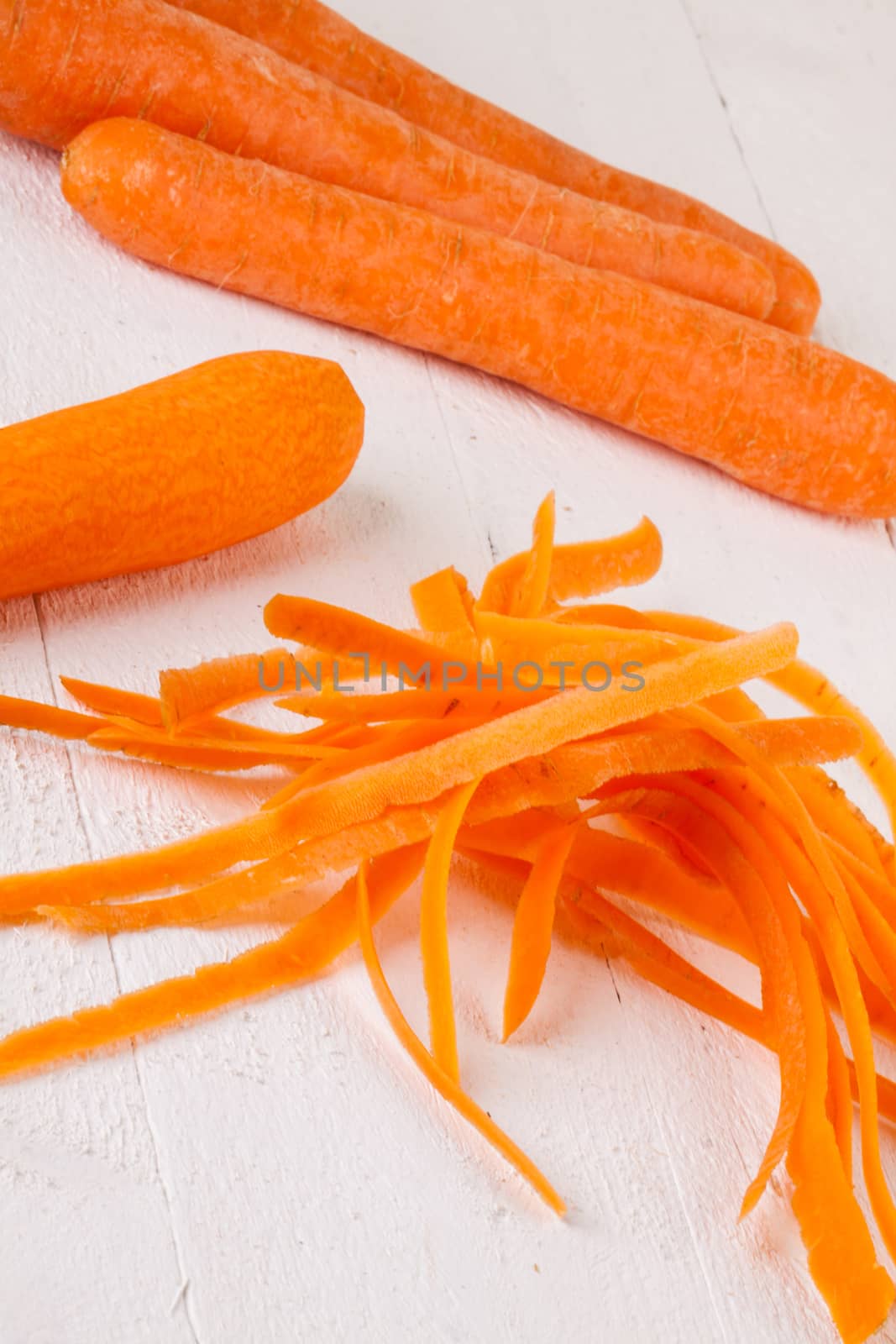 Fresh peeled carrots sliced into thin batons for carrot julienne with a metal kitchen cutter on a white background