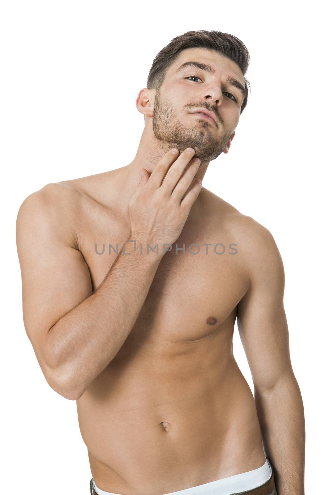 Handsome shirtless naked bearded young man standing looking intently at the camera with his hand to his chin in a sensual sexy pose, isolated on white