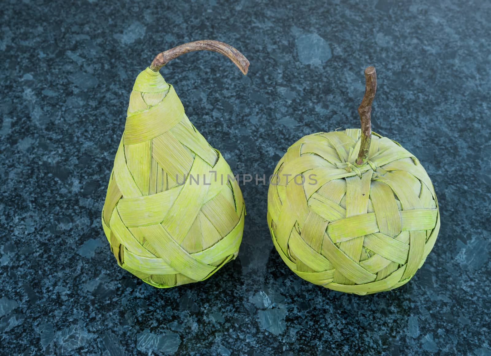 Green pear and apple made from bast fibre laying on the dark granite