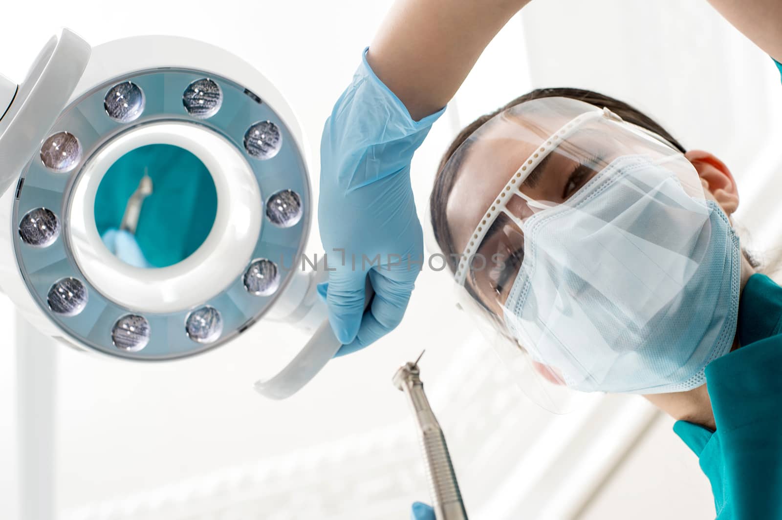 Surgical masked female dentist adjusting dental lamp