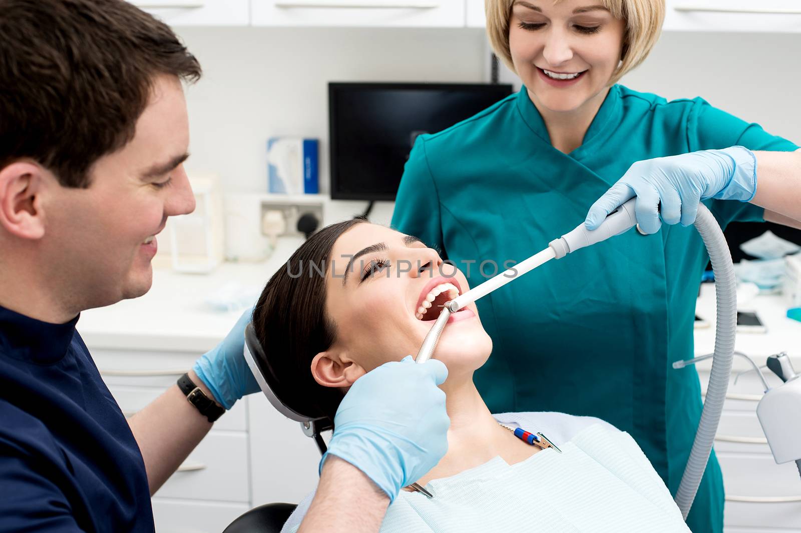 Male dentist treating patient teeth with assistant