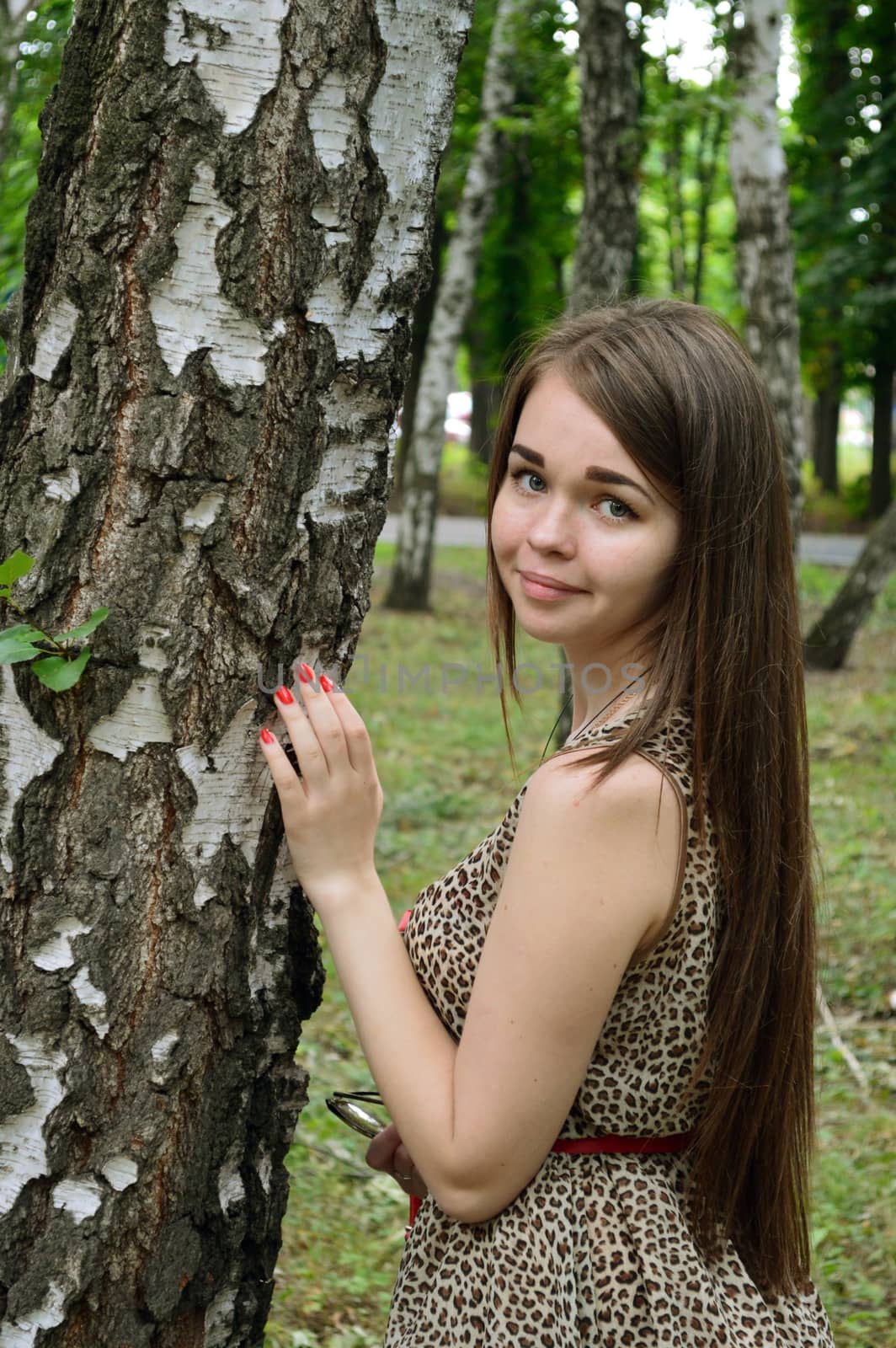 girl standing near birch on a background of blurred trees and greenery