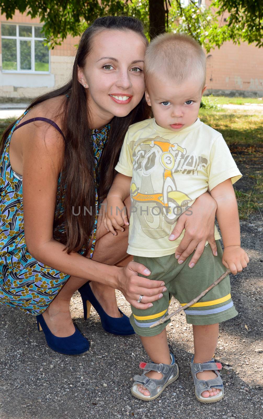 Mom and young son sitting on his haunches on the background of foliage and walls