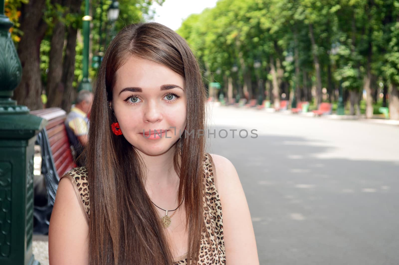 Portrait of a young girl sitting in a park on a background of green trees and alleys