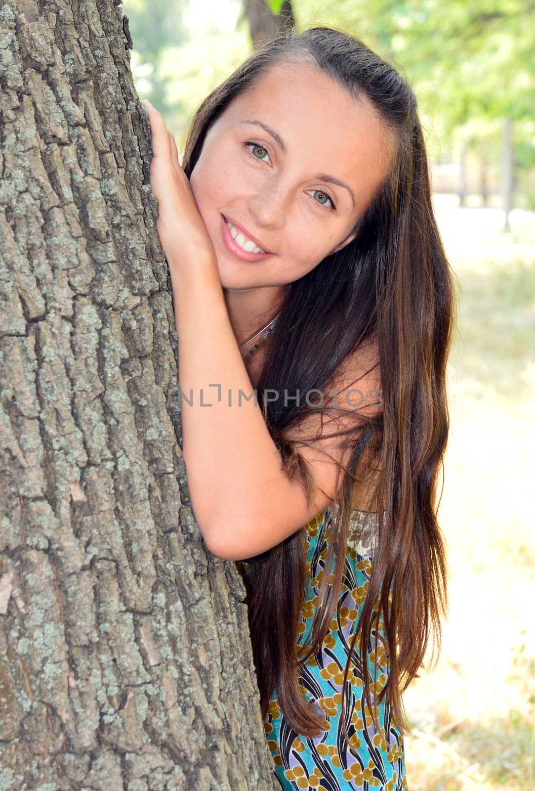 Portrait of a young girl hid behind a tree trunk