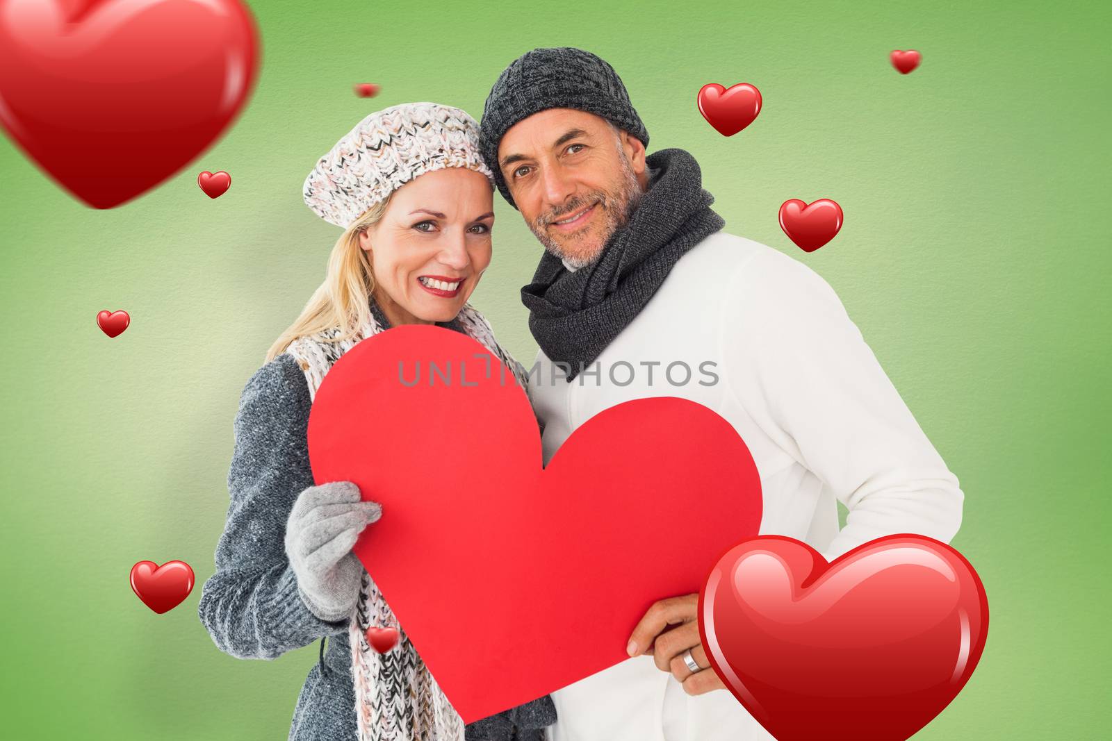 Smiling couple in winter fashion posing with heart shape against green vignette