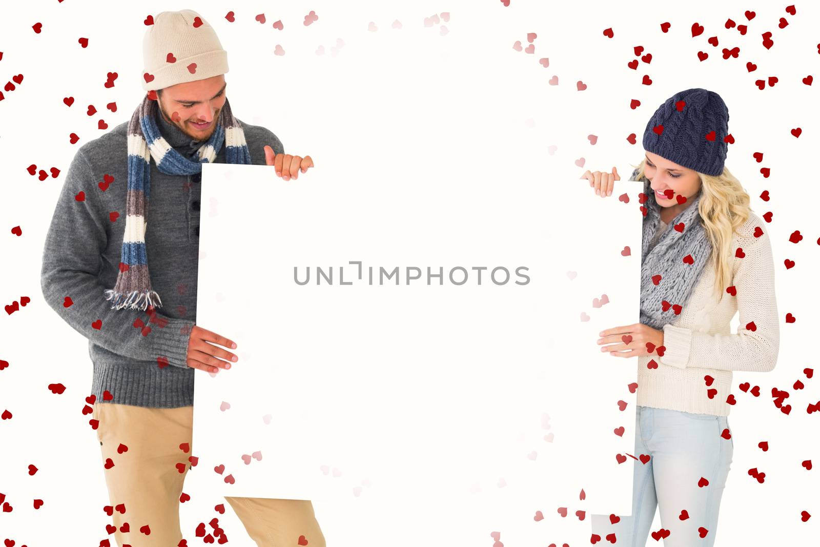 Attractive couple in winter fashion showing poster against red love hearts
