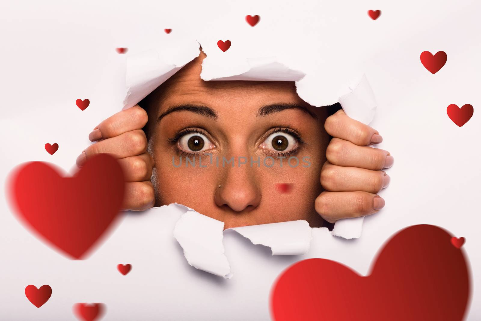 Young woman looking through paper rip against hearts